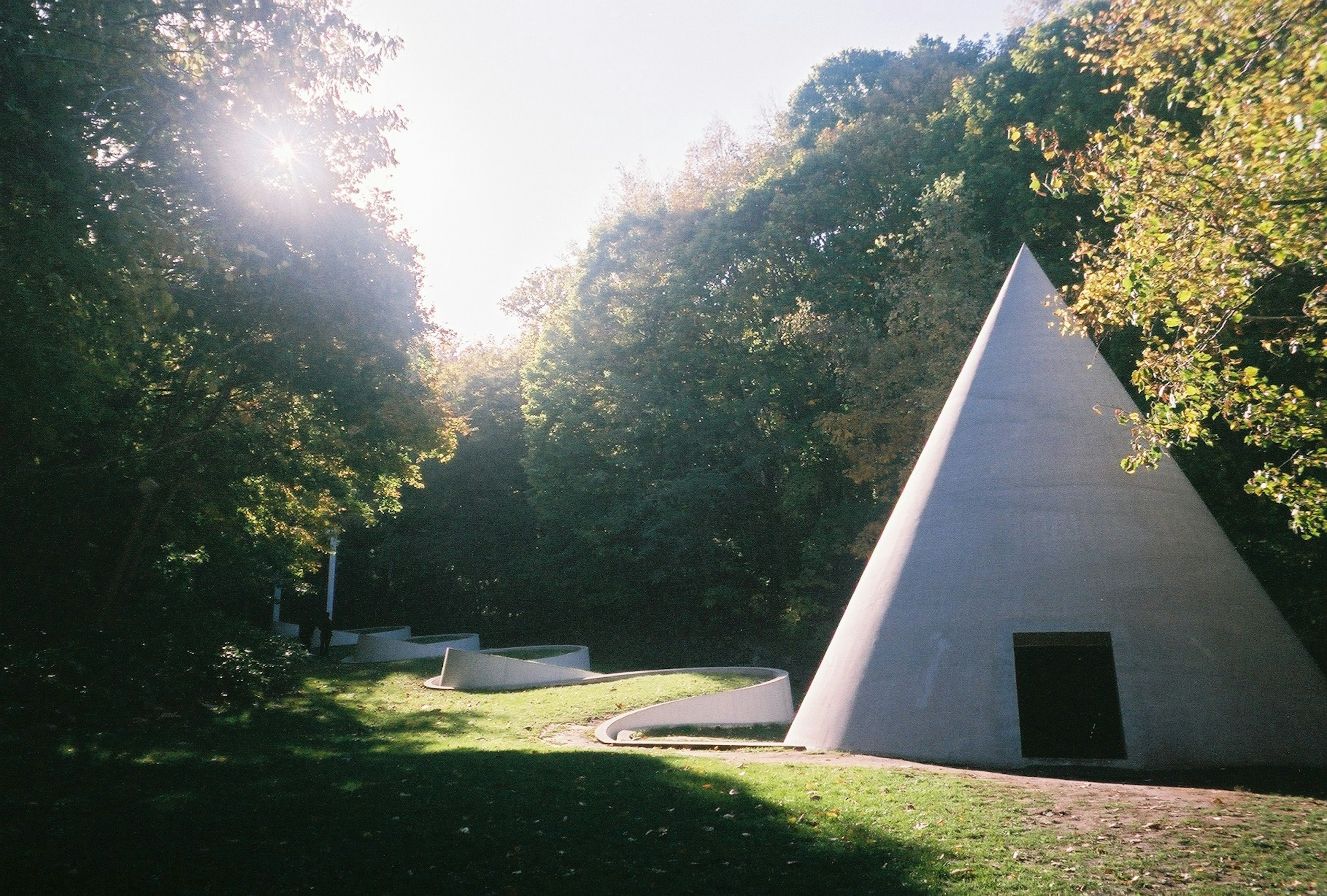 Bâtiment en forme de pyramide blanche entouré d'arbres verts et de lumière douce