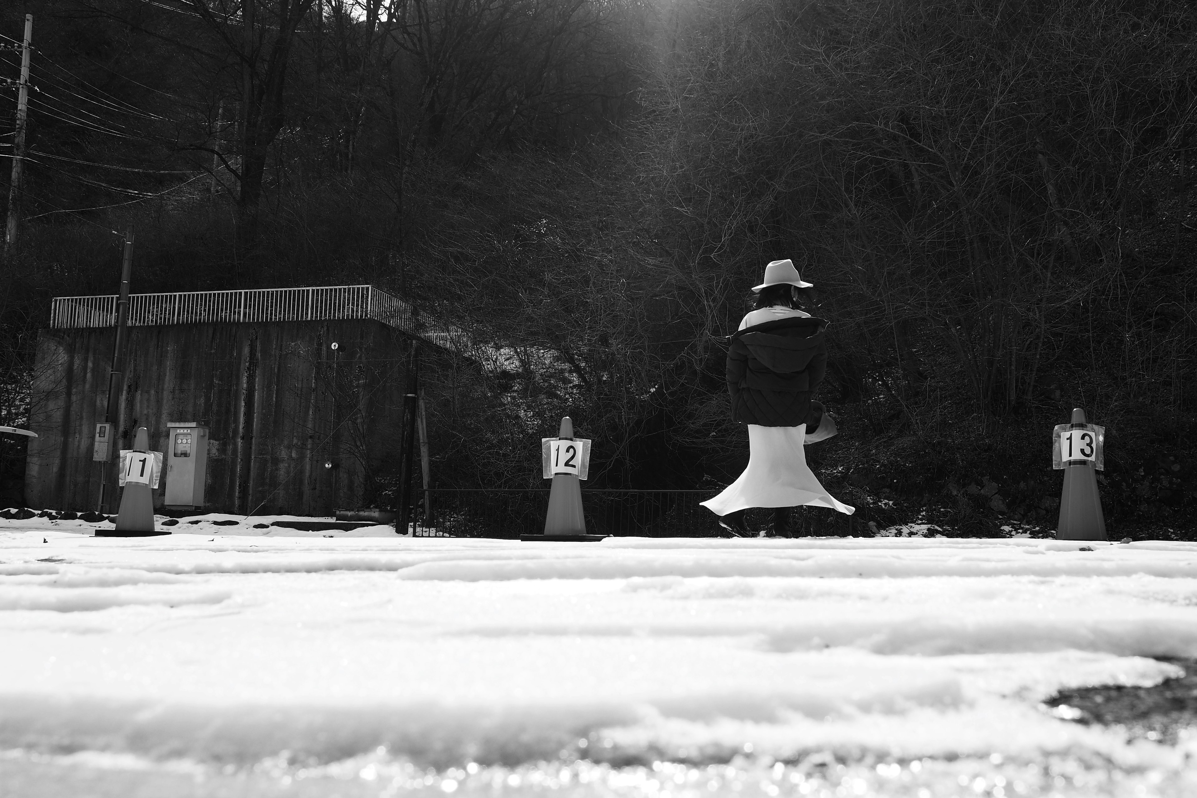 白黒の雪の上に立つ人物と小屋の風景