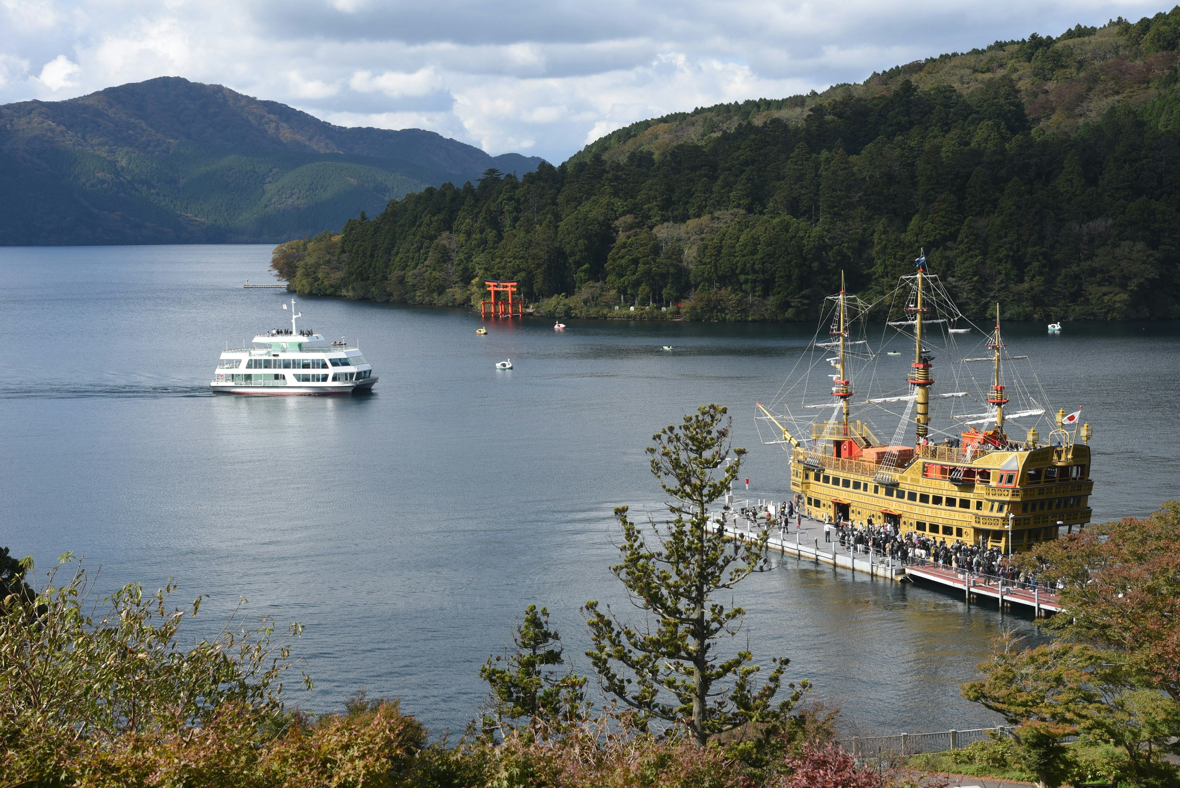 Gelbes Piratenschiff und weißes Kreuzfahrtschiff auf dem See umgeben von Bergen