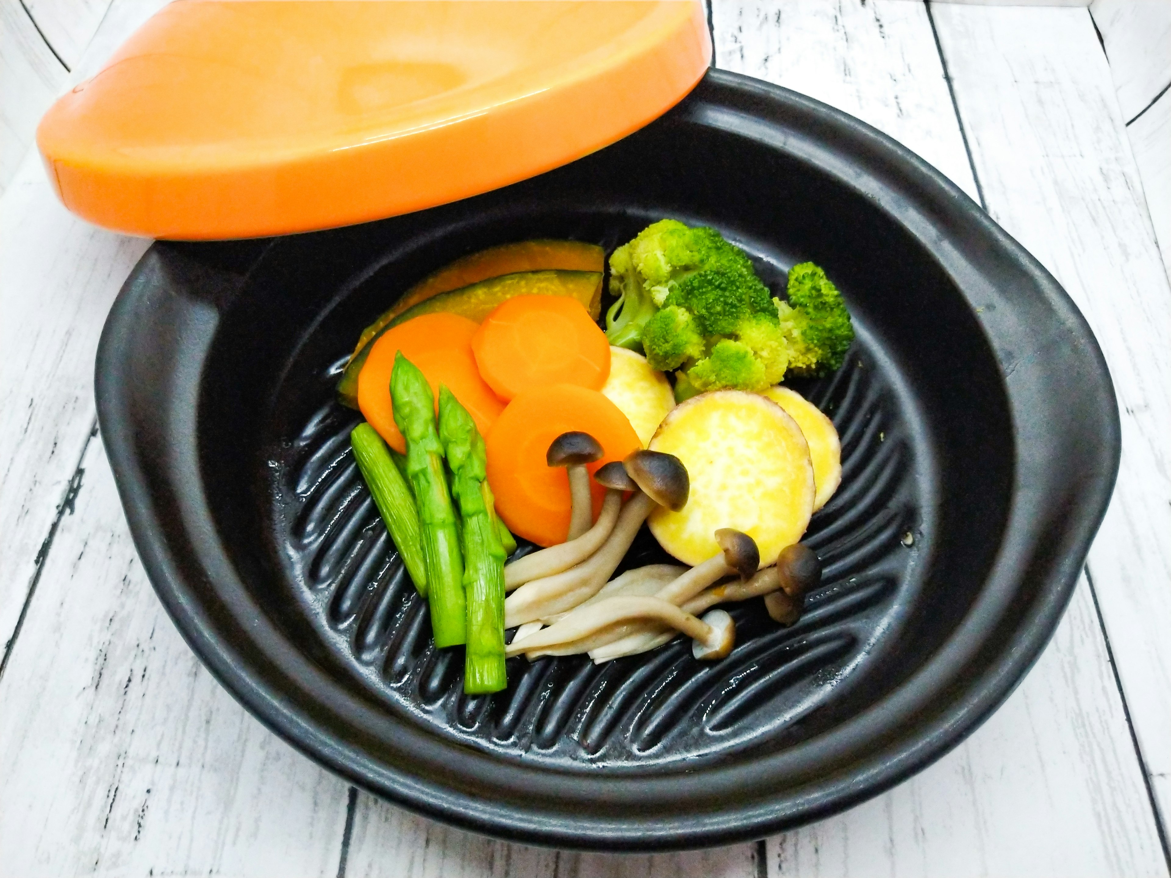 Colorful vegetables arranged in a black dish with an orange lid