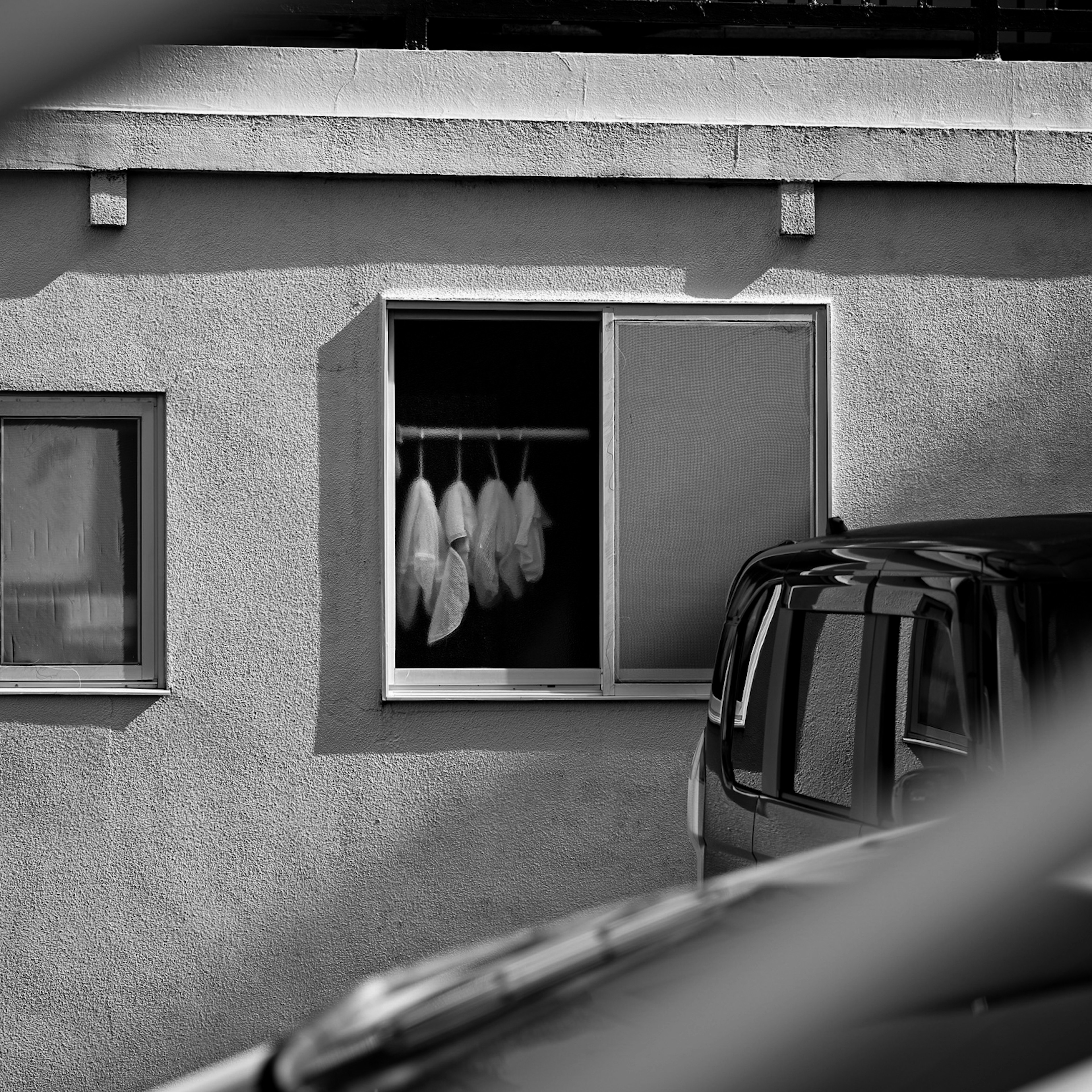 Schwarzweißfoto eines Fensters mit Kleidung, die an einem Kleiderbügel hängt