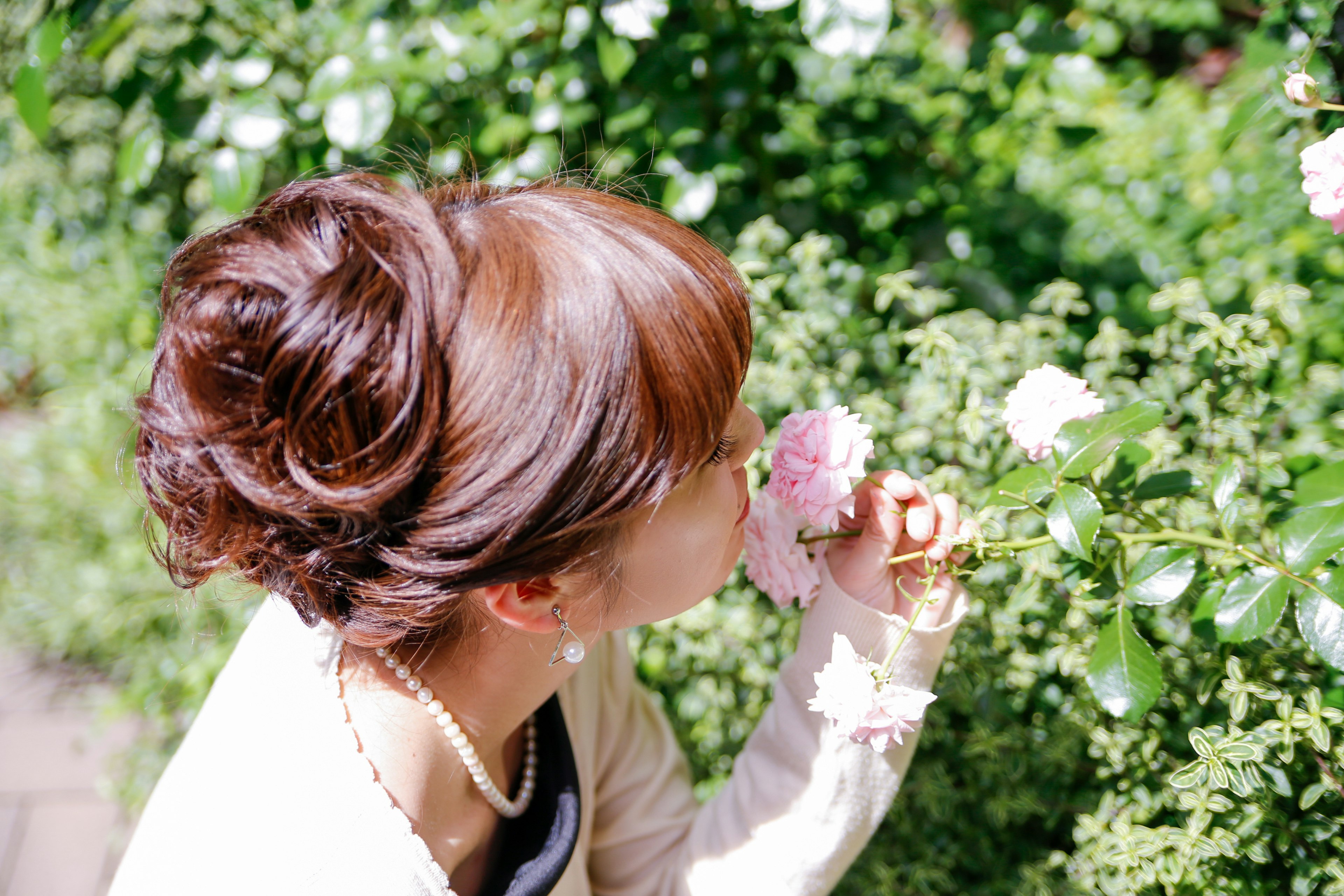 A woman smelling a pink rose surrounded by green foliage