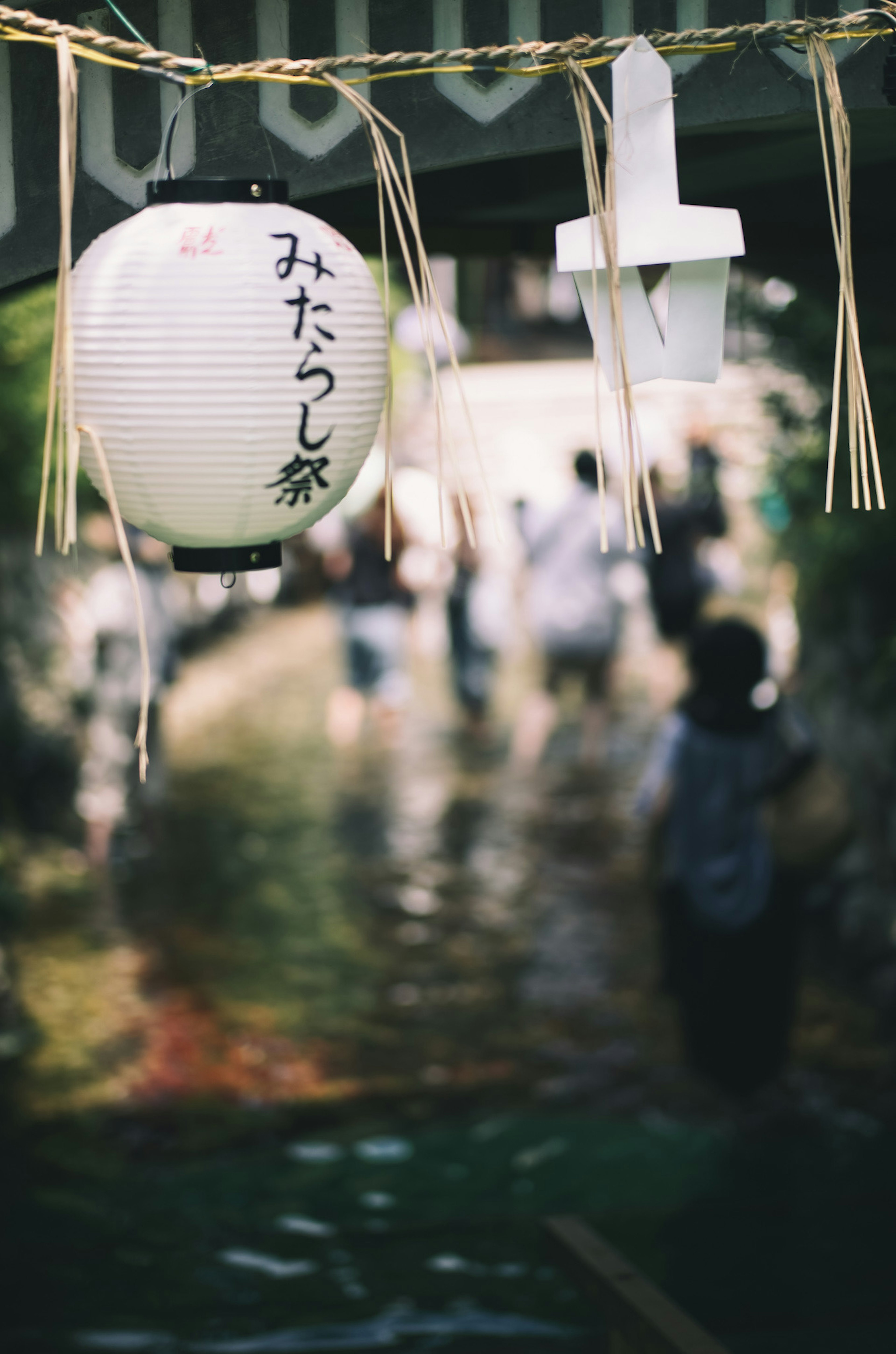 A lantern hanging by the water with silhouettes of people in the background