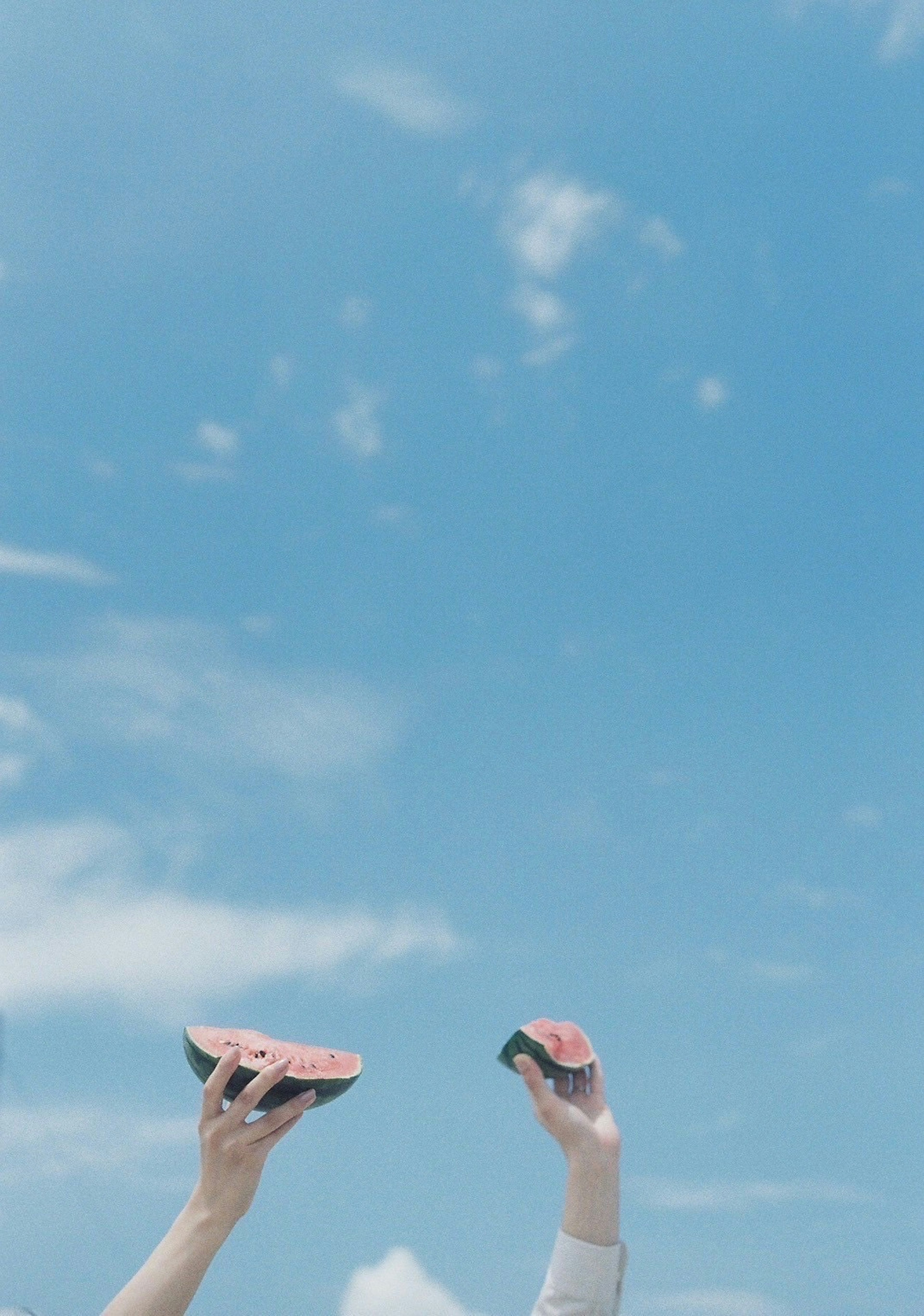 Two hands holding watermelon slices under a blue sky