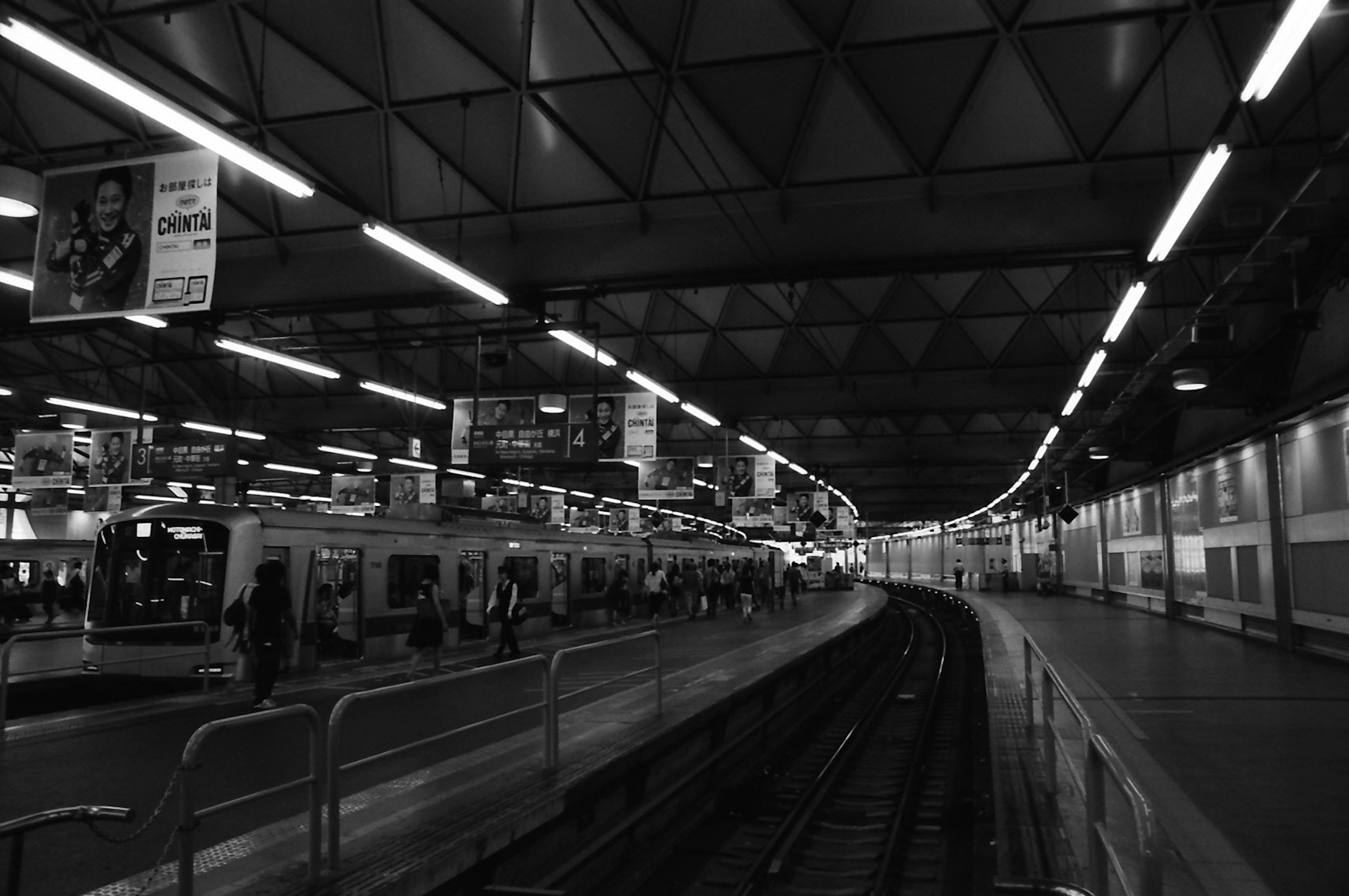 Foto en blanco y negro de una estación de tren con andenes y vías curvas