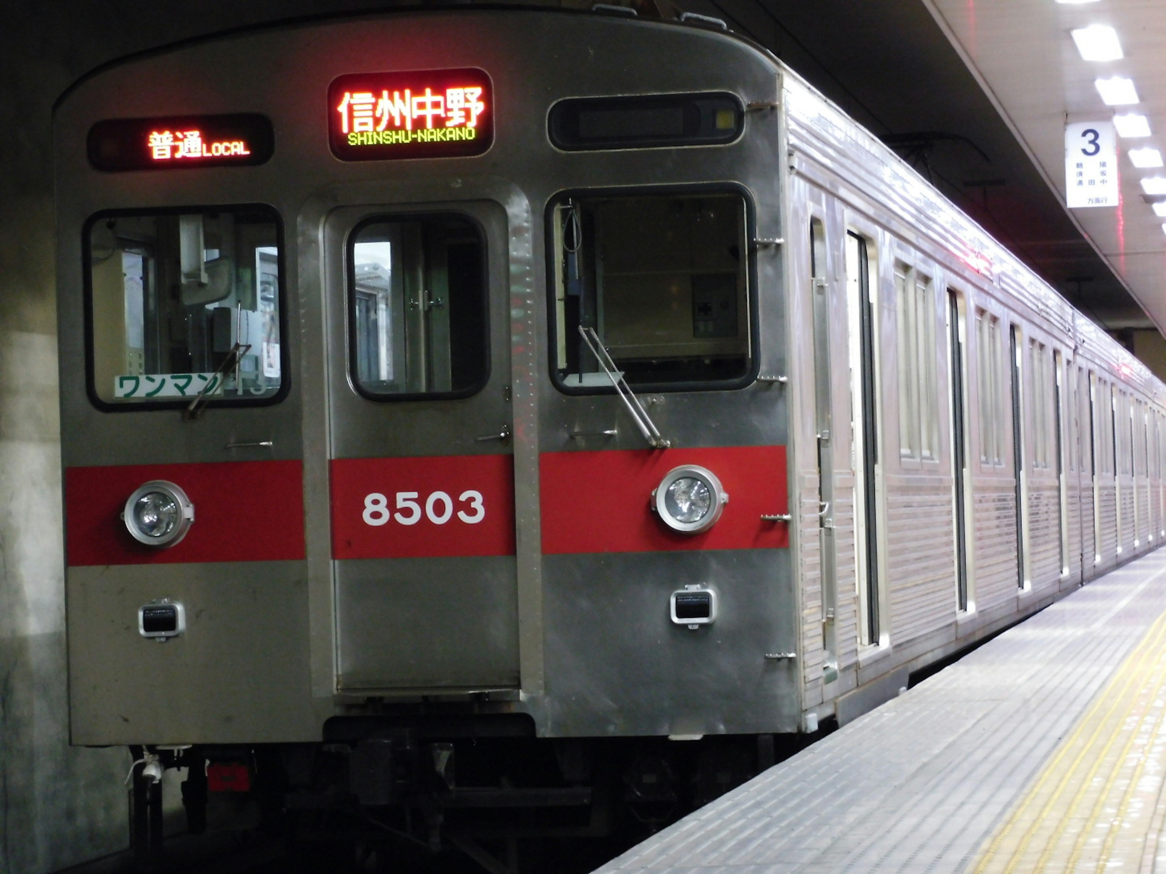 Silver train with red stripe stopped at a station