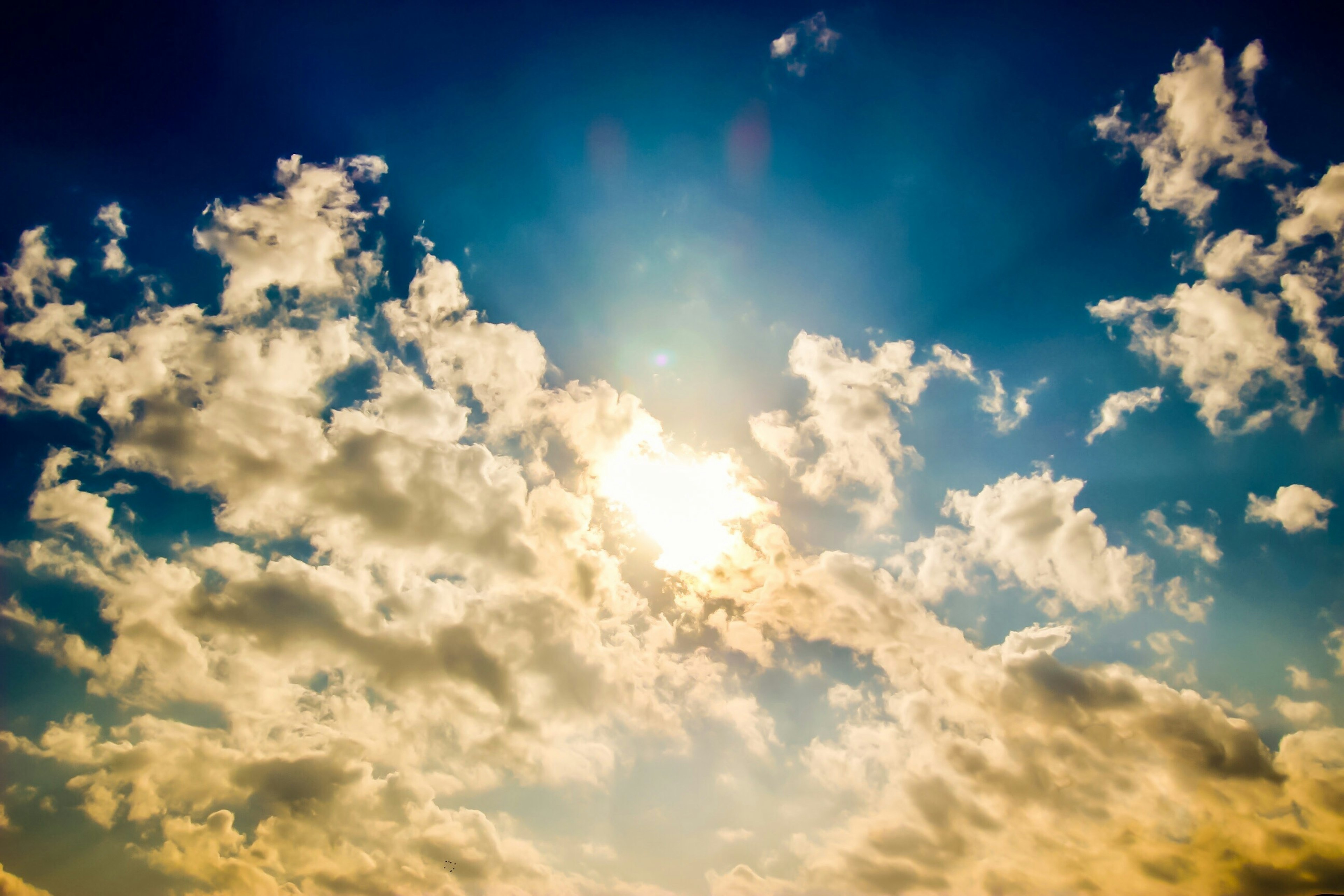 A blue sky with fluffy white clouds and sunlight streaming through