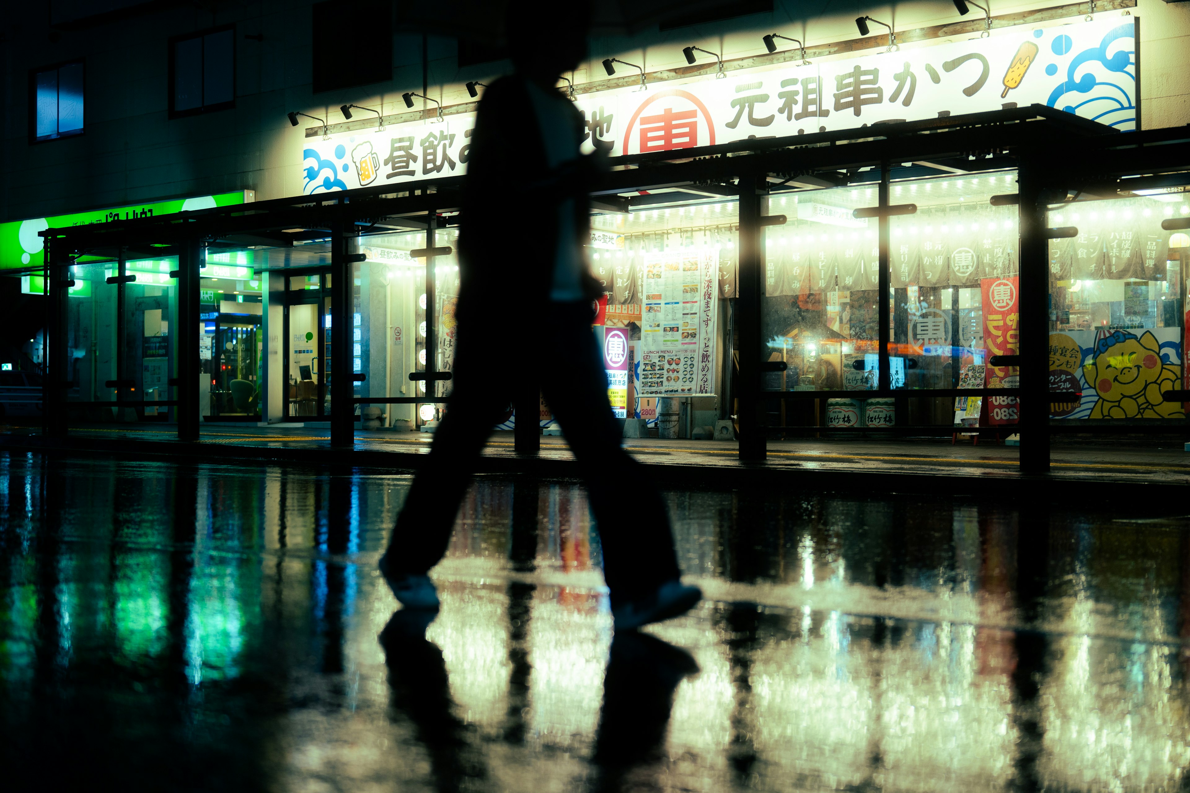 Silhouette of a person walking in the night Reflecting puddles on the road Store lights glowing