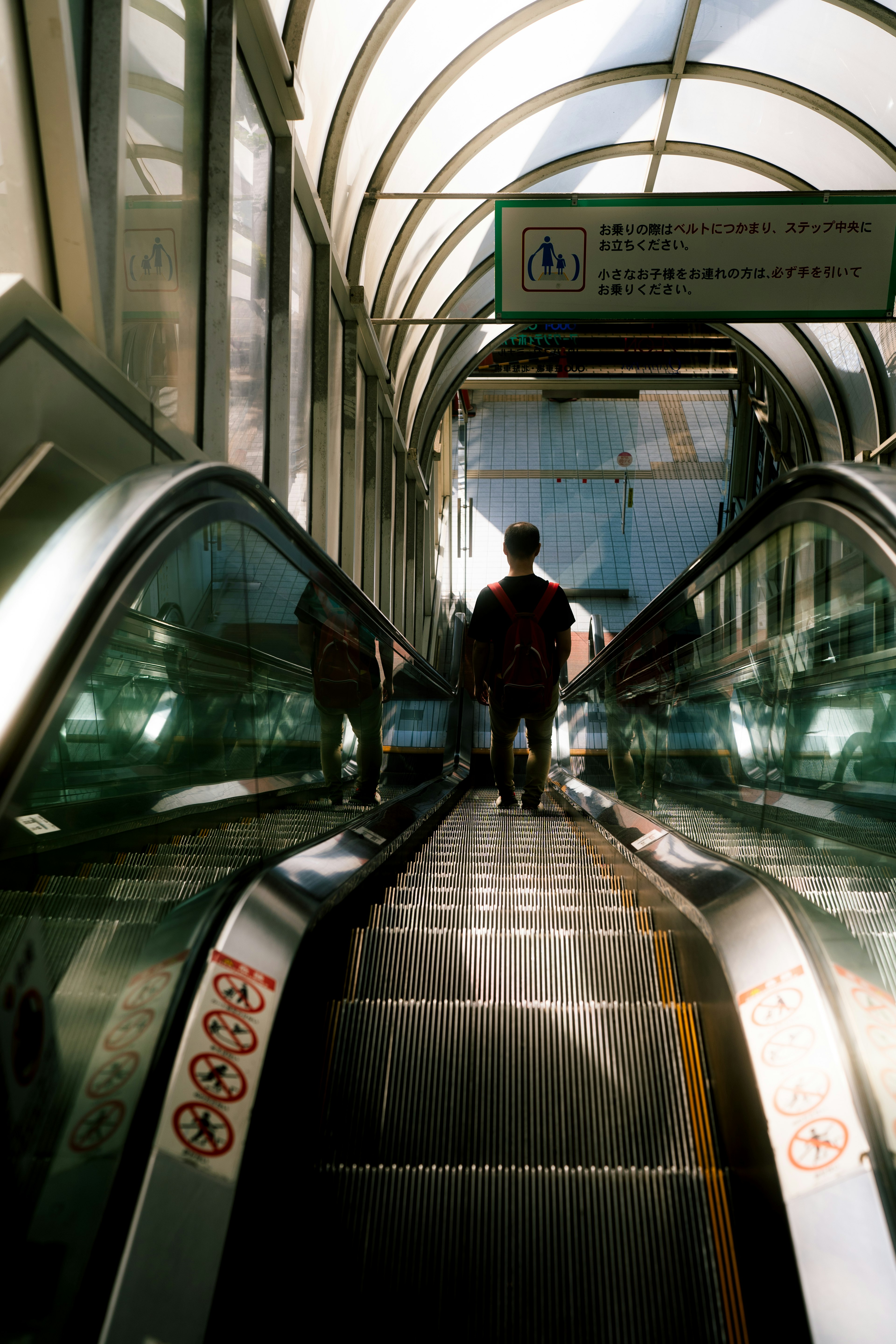 Person descending an escalator under a bright glass roof structure