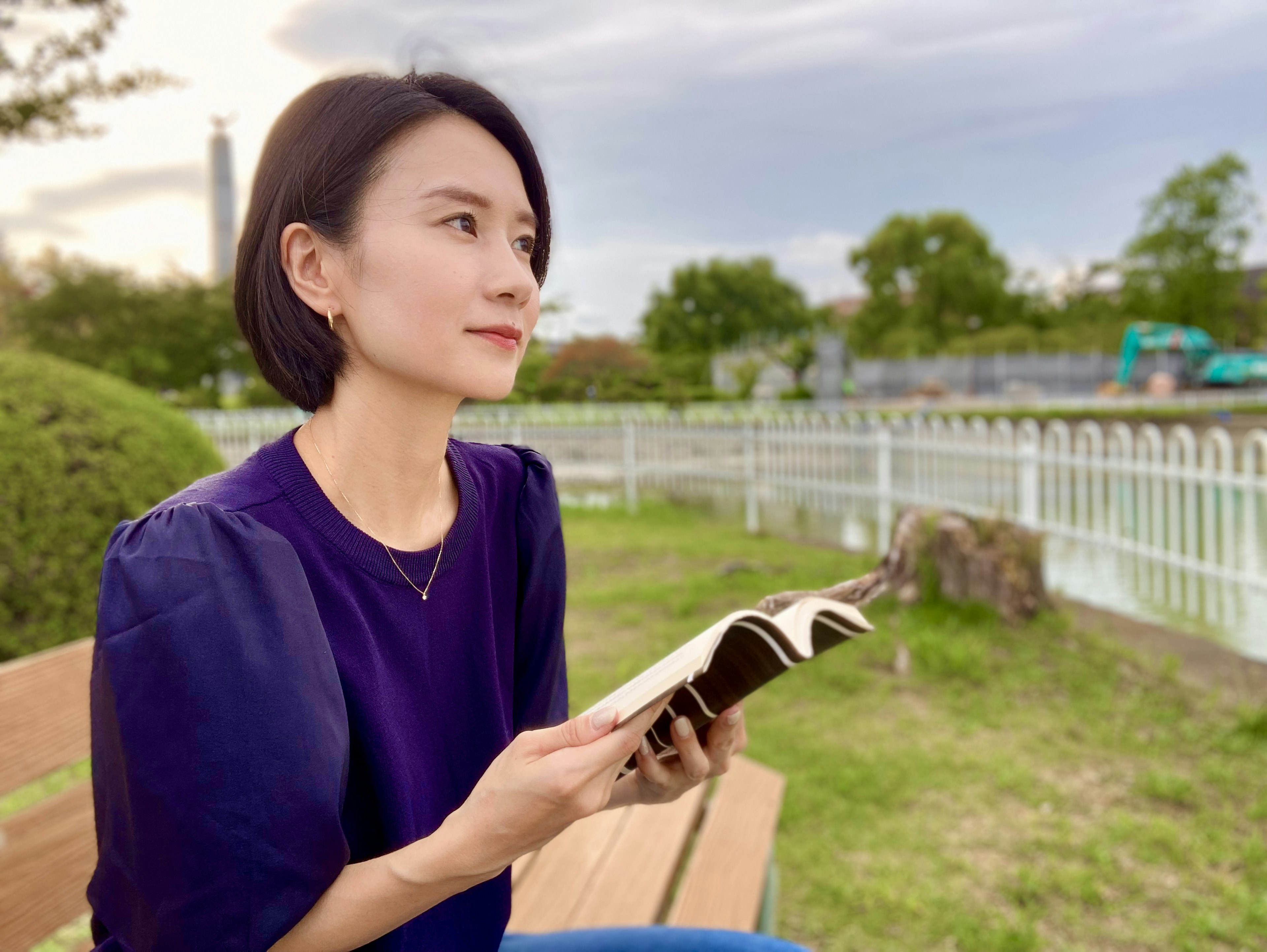 Woman sitting on a park bench holding a book soft evening light