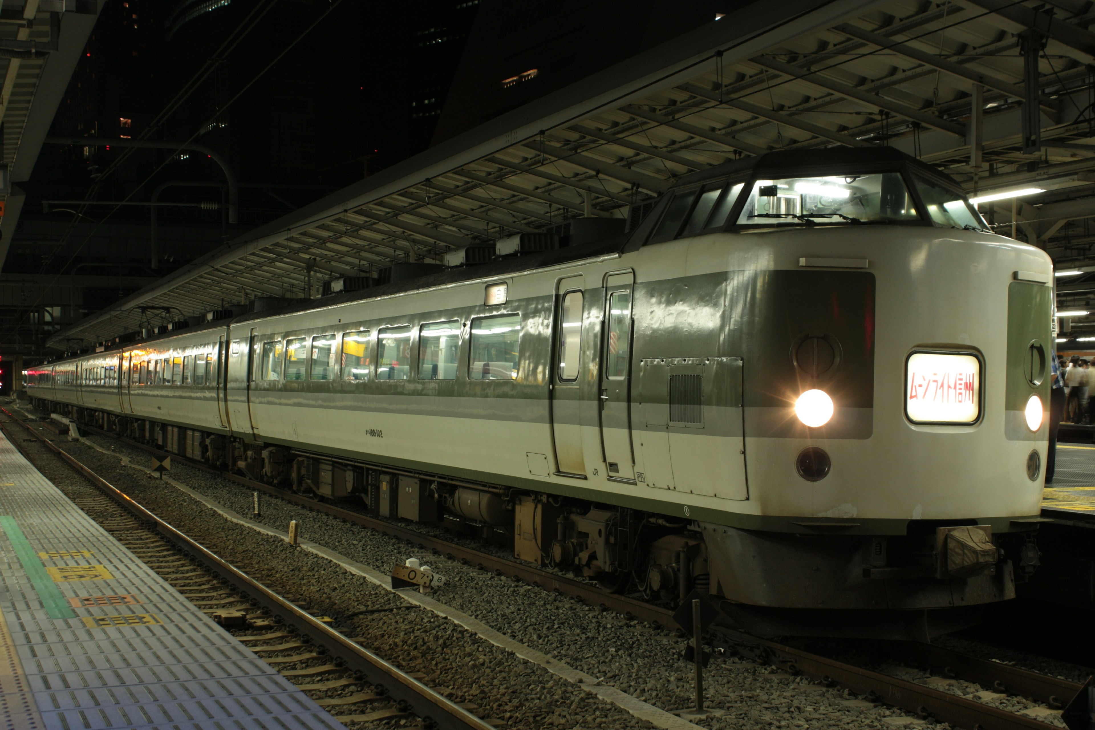 A white and green train stopped at a station at night