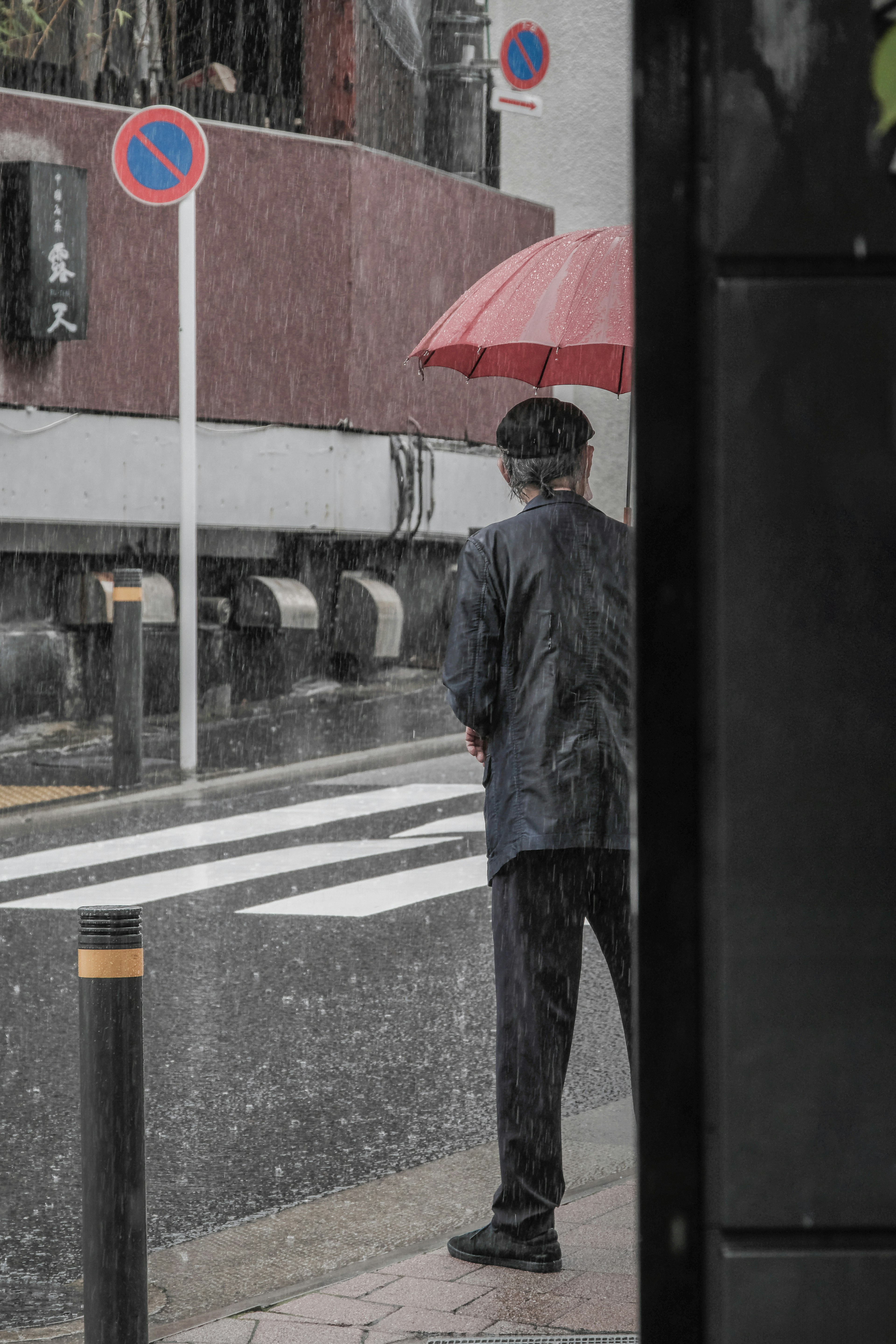 一个男人在雨中站在斑马线附近，手里拿着红色雨伞