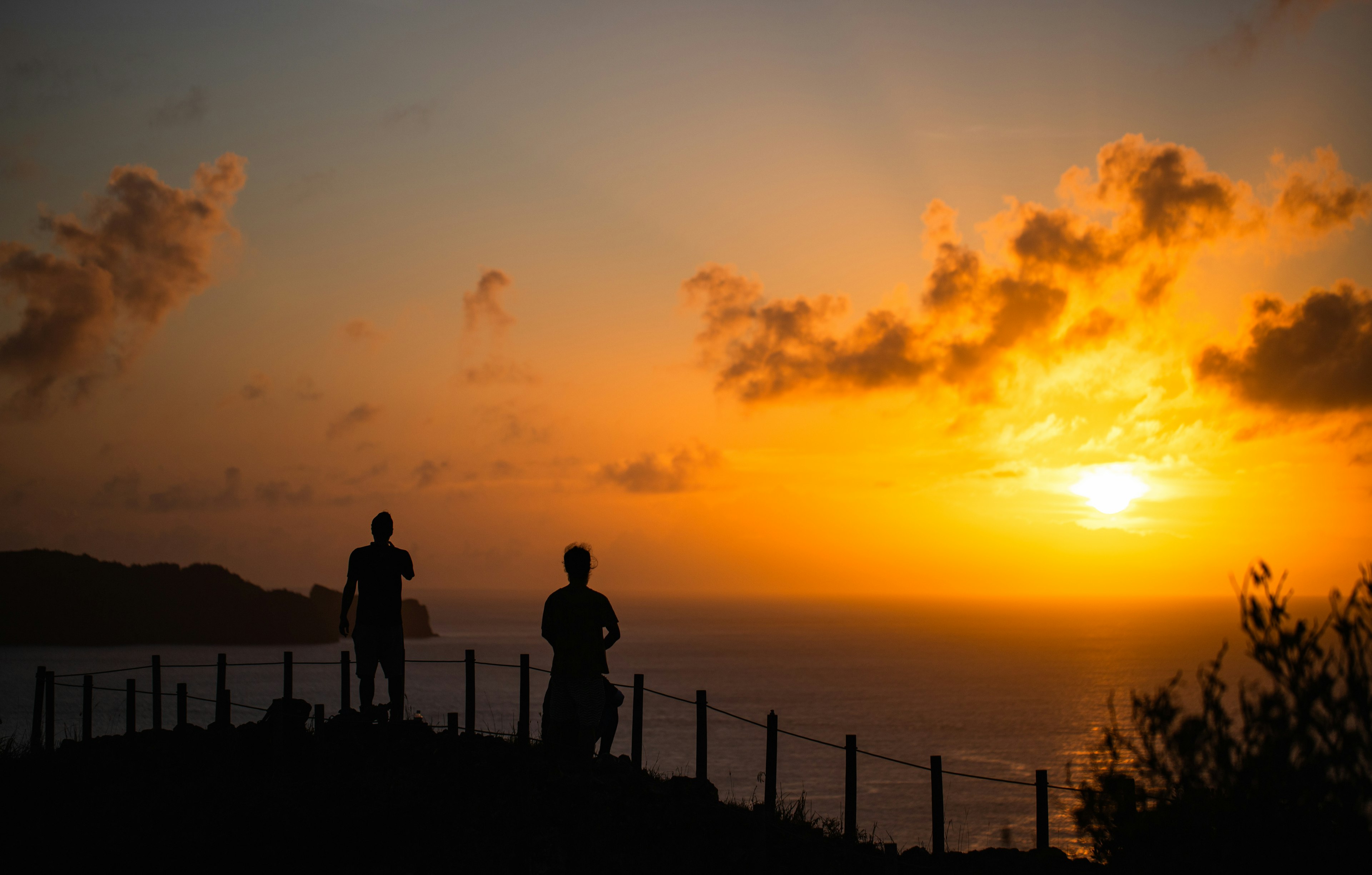 夕日を背にした二人のシルエットが海を見つめる風景