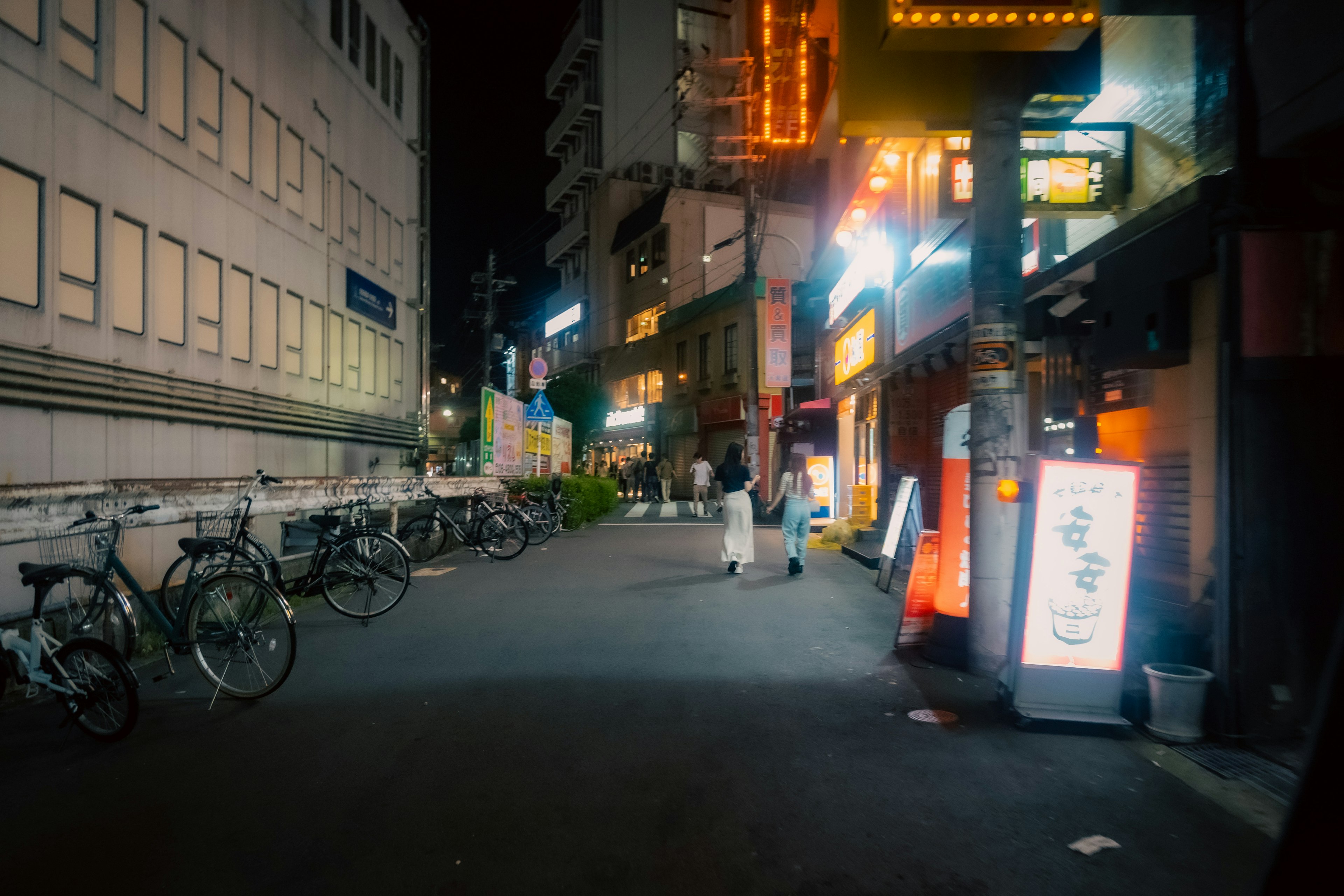 Scène de rue nocturne avec des vélos garés et des enseignes lumineuses