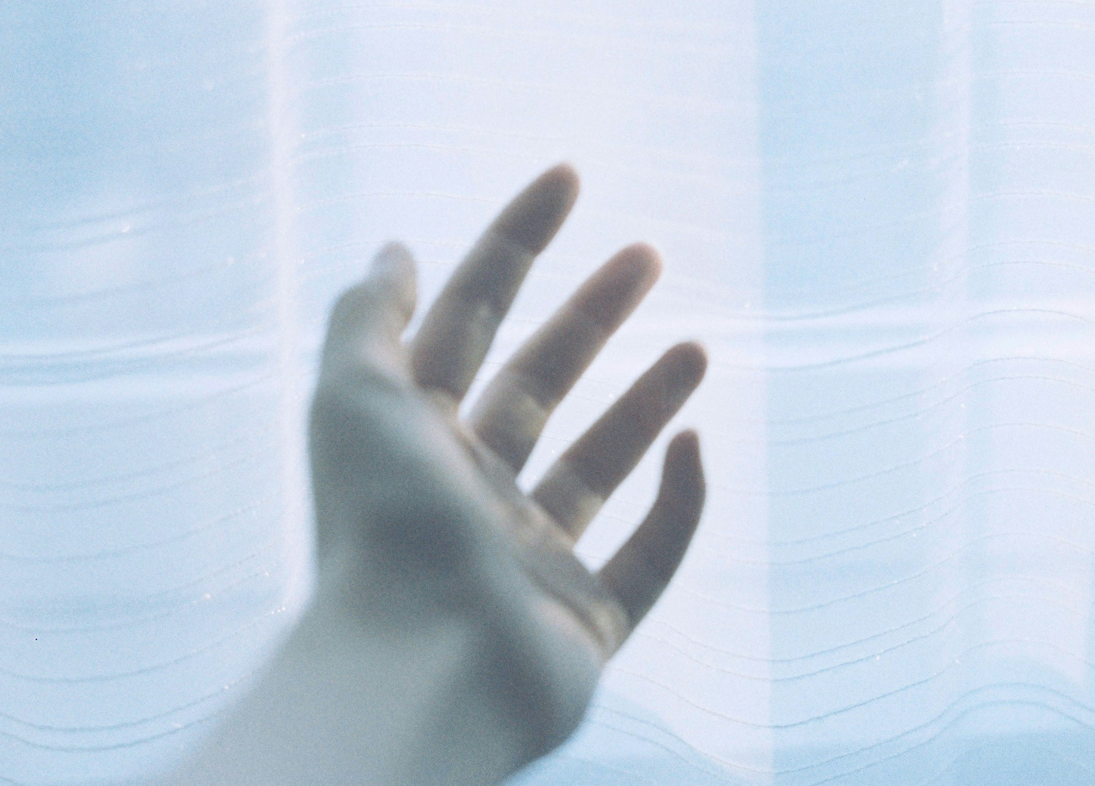 A hand reaching out through sheer curtains