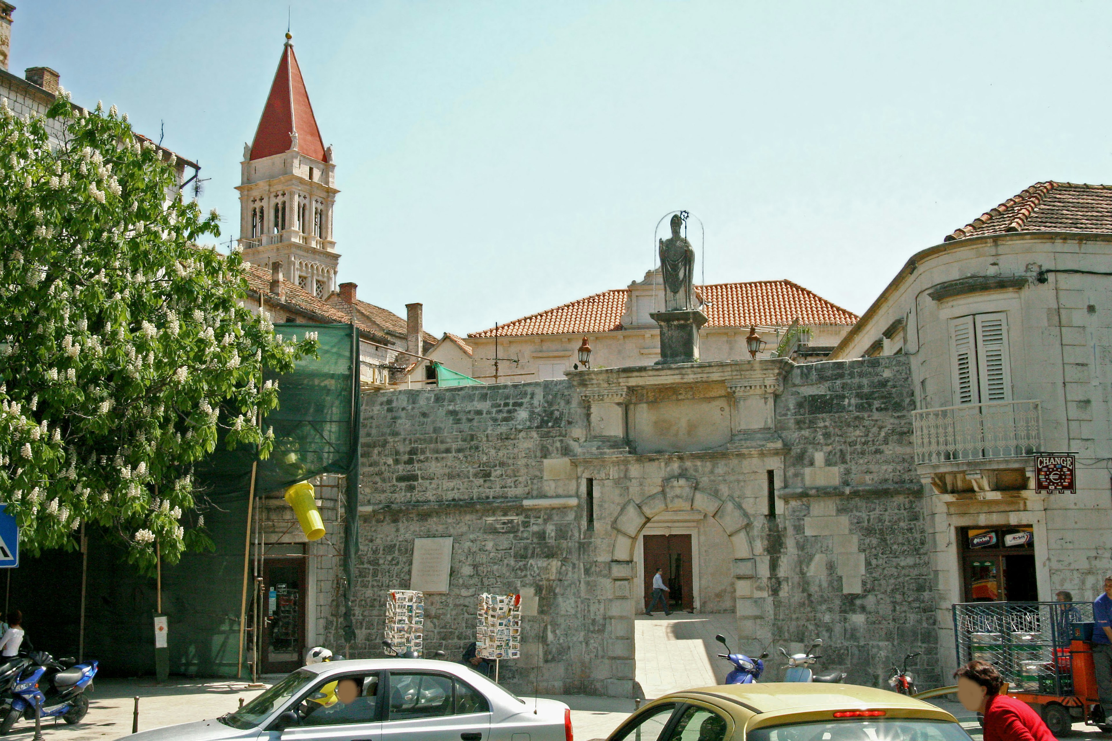 View of an old stone building with a tower and statue in a square