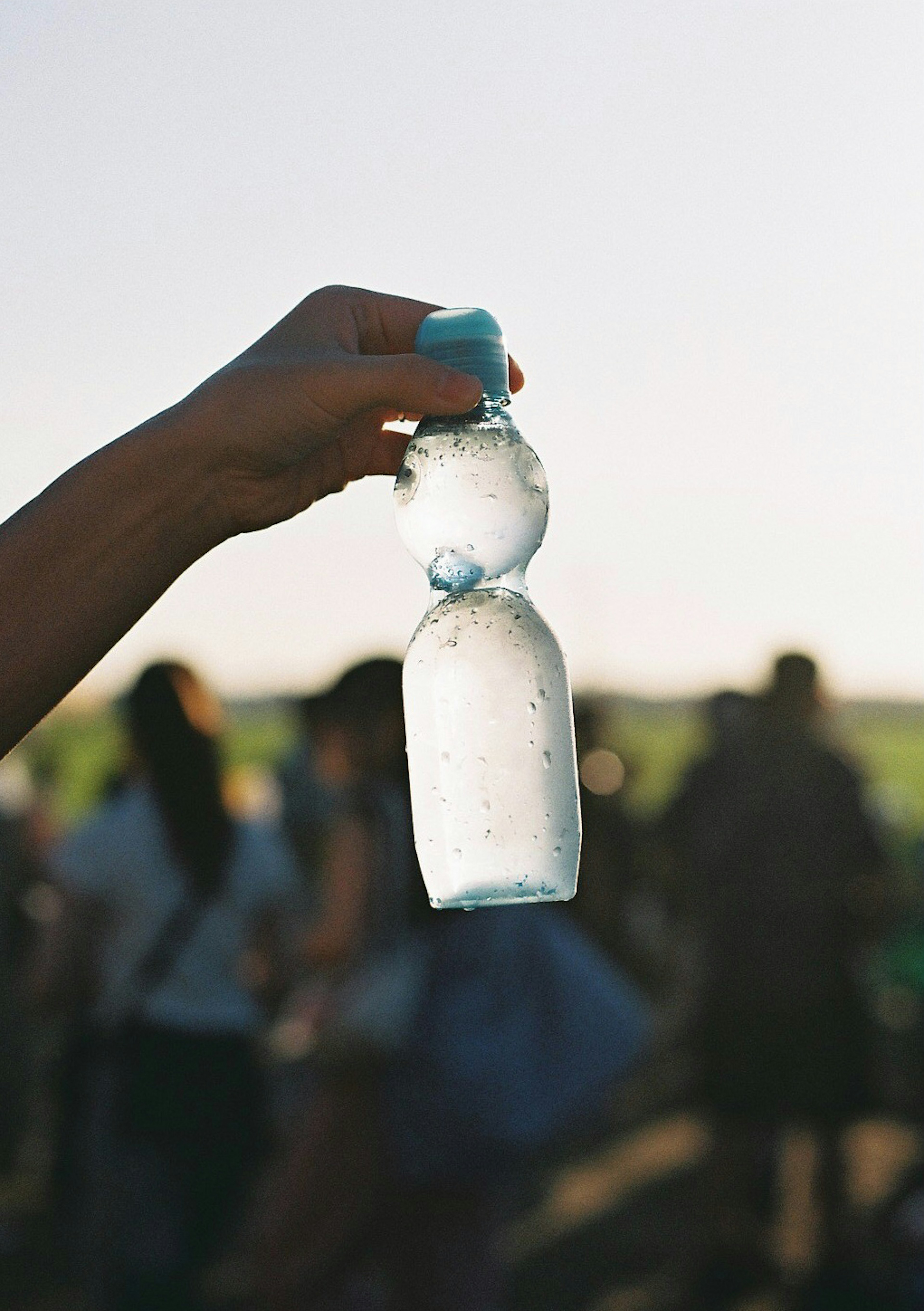 Eine Hand hält eine transparente Wasserflasche mit einem blauen Deckel vor einer Menschenmenge