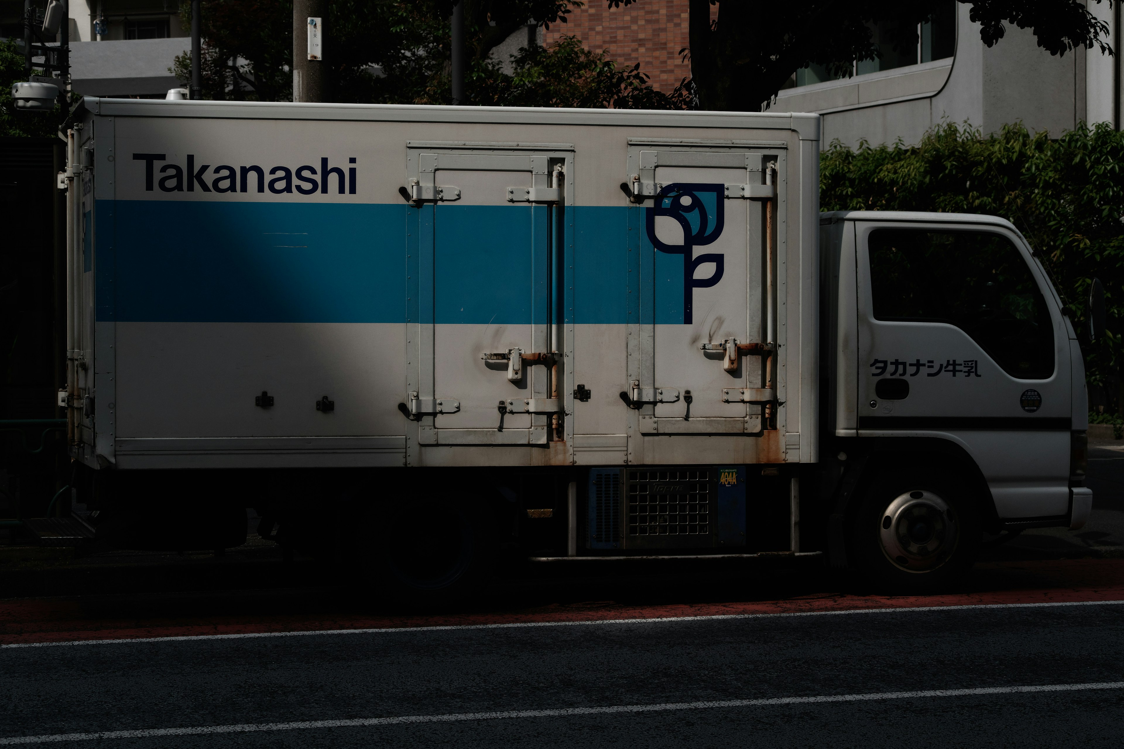 Un camion con strisce blu parcheggiato per strada con il marchio Takanashi