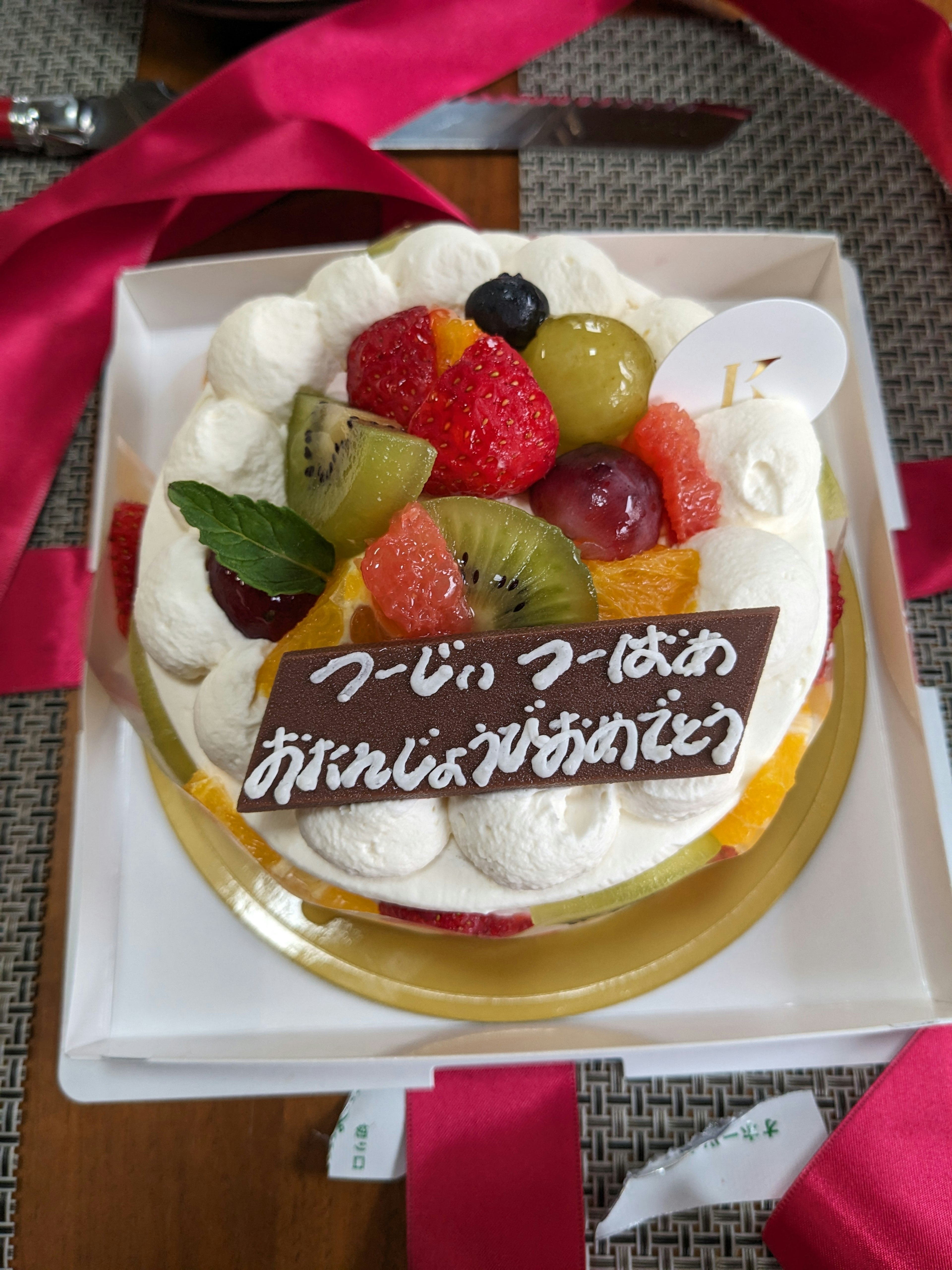 Una torta decorata con frutta e panna con una placca di messaggio