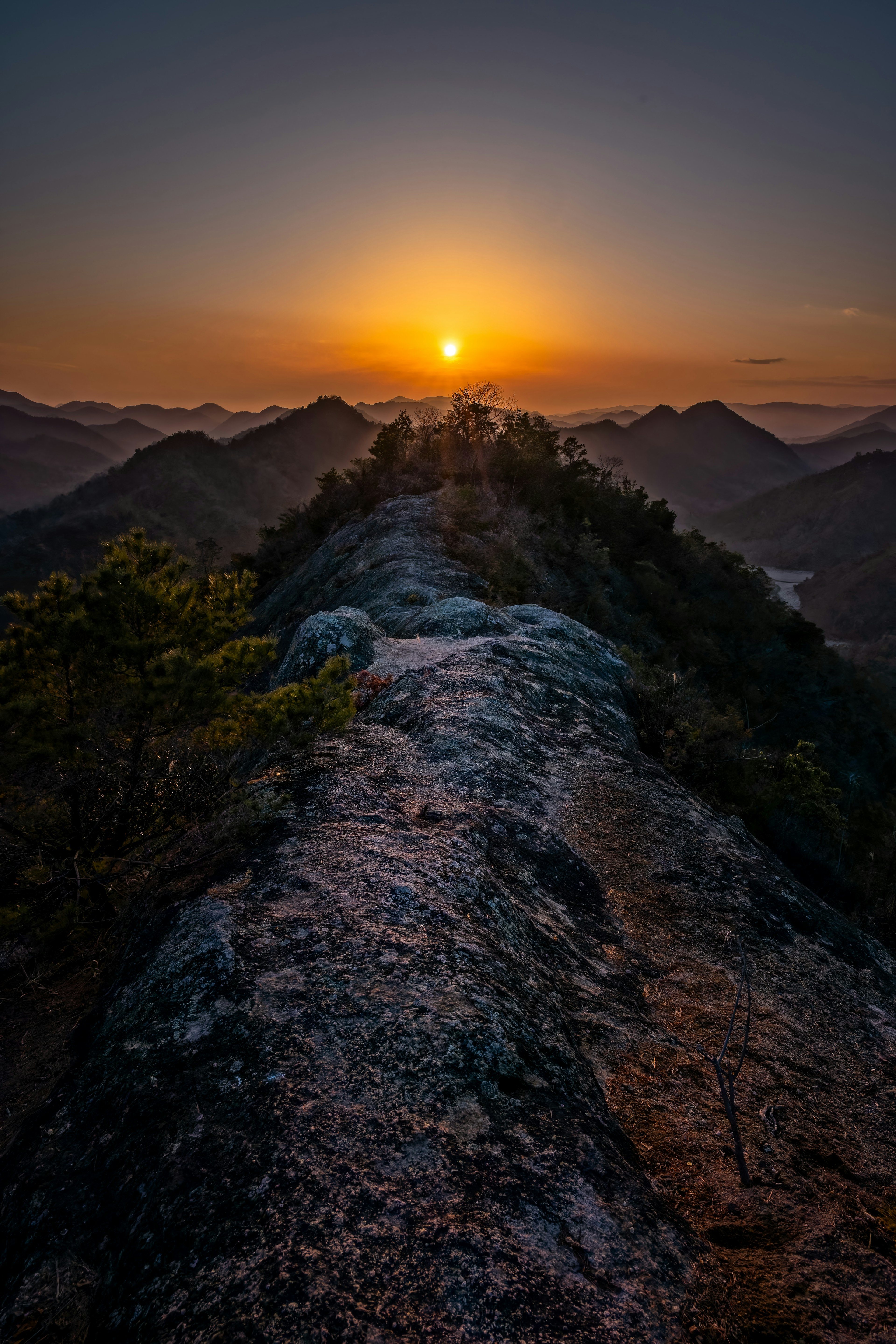 Blick von einem felsigen Grat bei Sonnenuntergang mit Bergen im Hintergrund