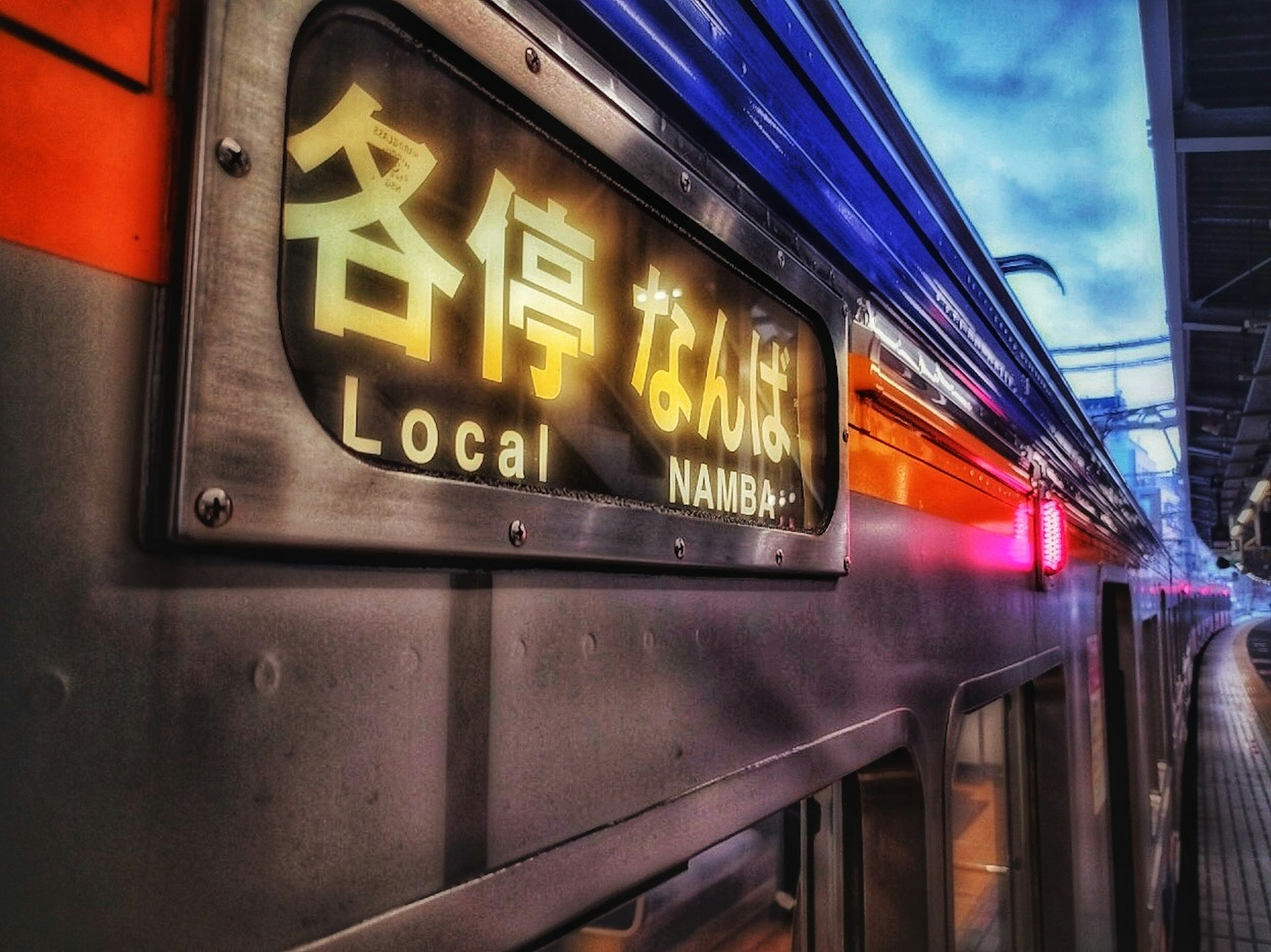 Train sign displaying Namba Local with vibrant night station ambiance