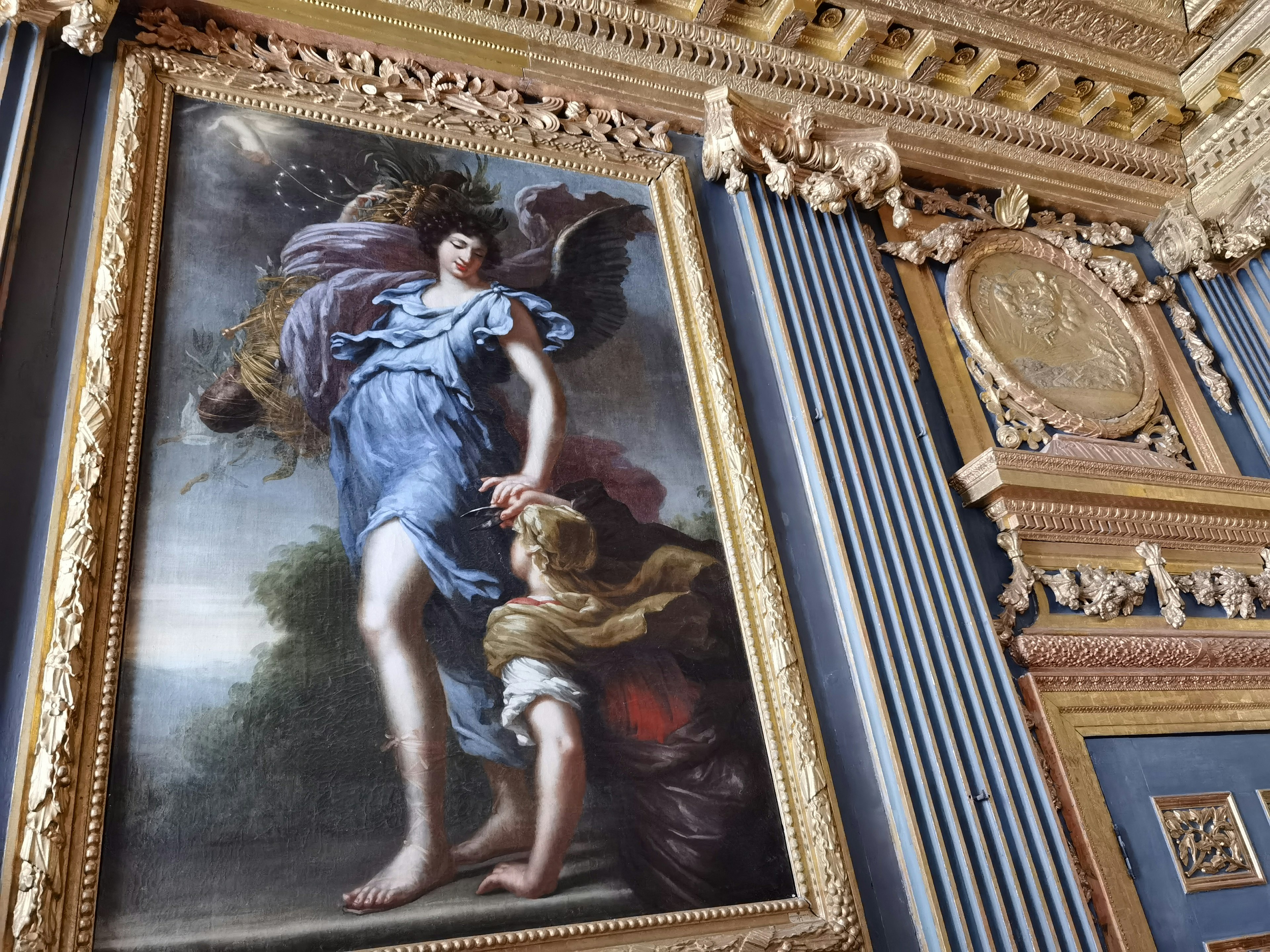 Une belle peinture entourée d'un cadre doré orné sur un mur avec une femme en robe bleue et un enfant