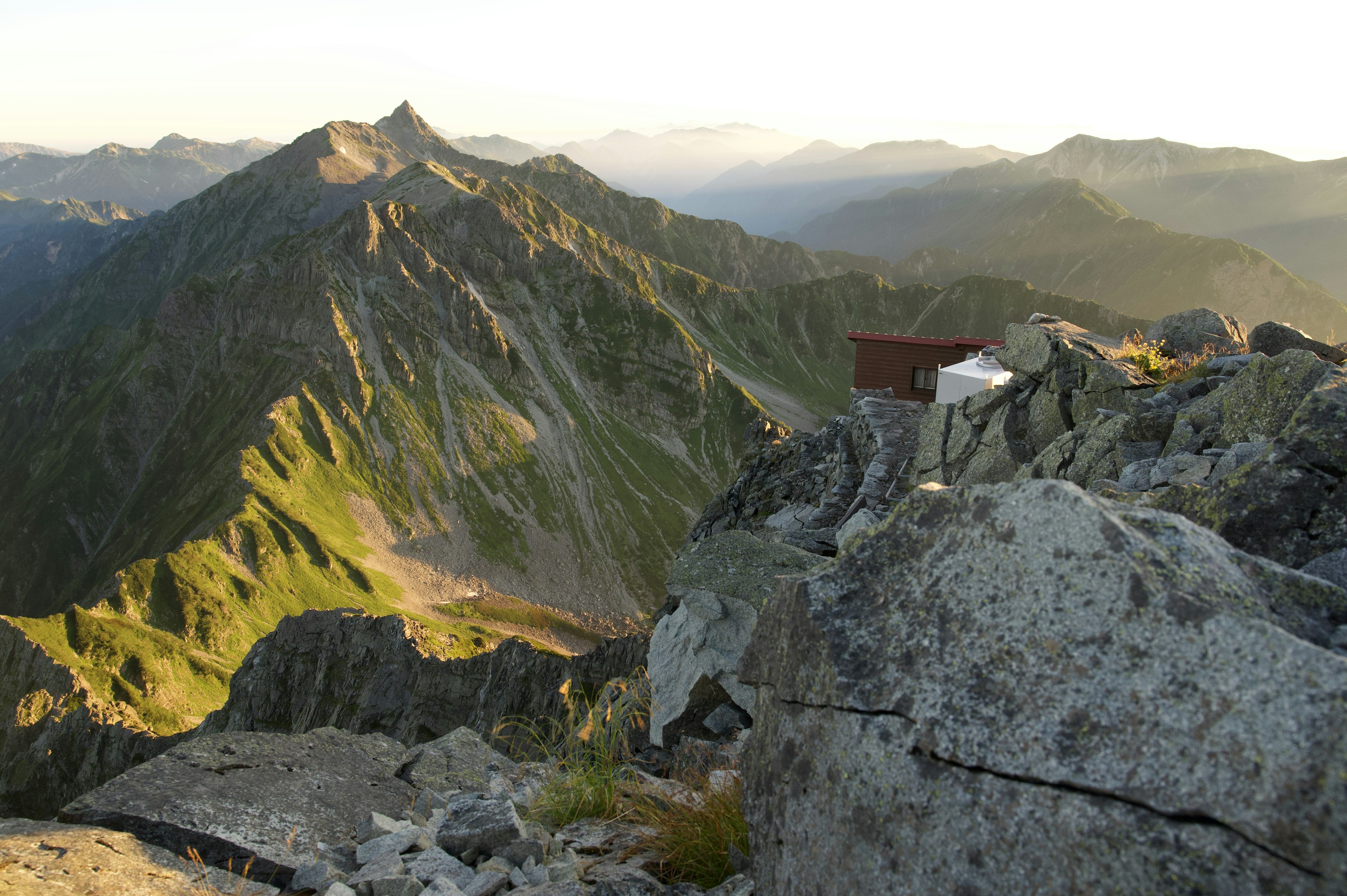 Vue panoramique depuis un sommet de montagne montrant des pentes vertes et un terrain rocheux