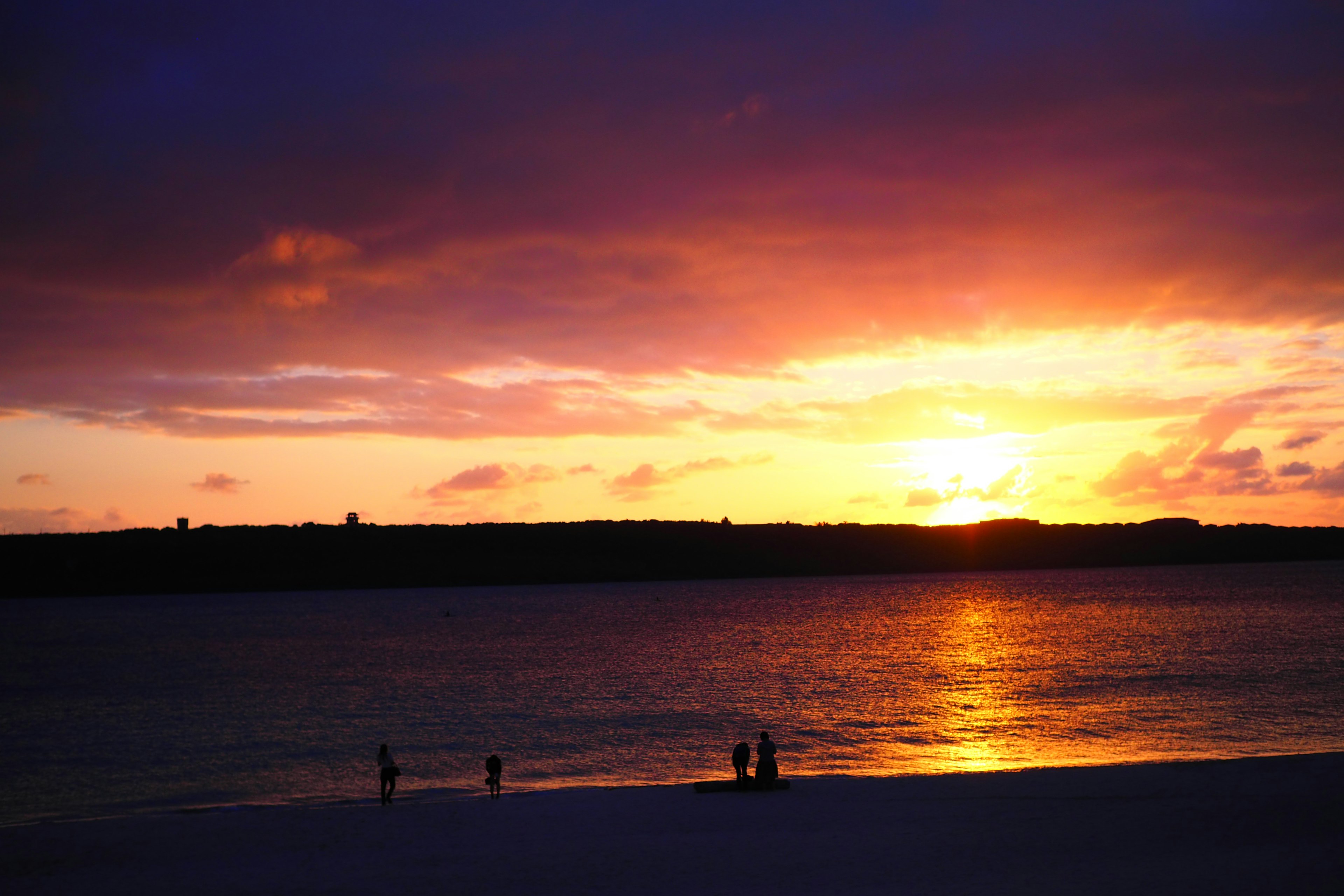 Silhouette di persone sulla spiaggia al tramonto con cielo arancione e viola vibrante