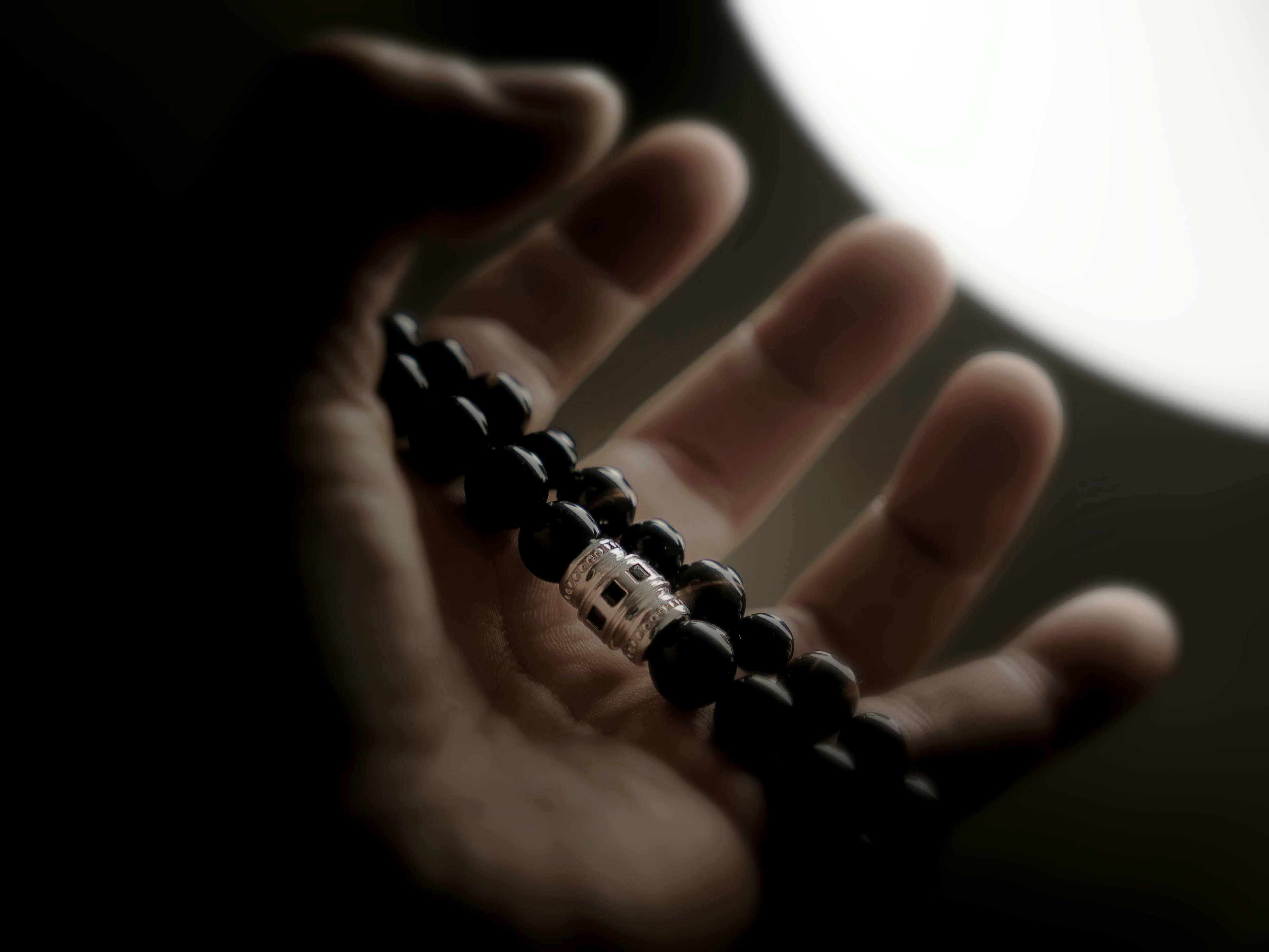 A hand holding a black bead bracelet with a bright light in the background