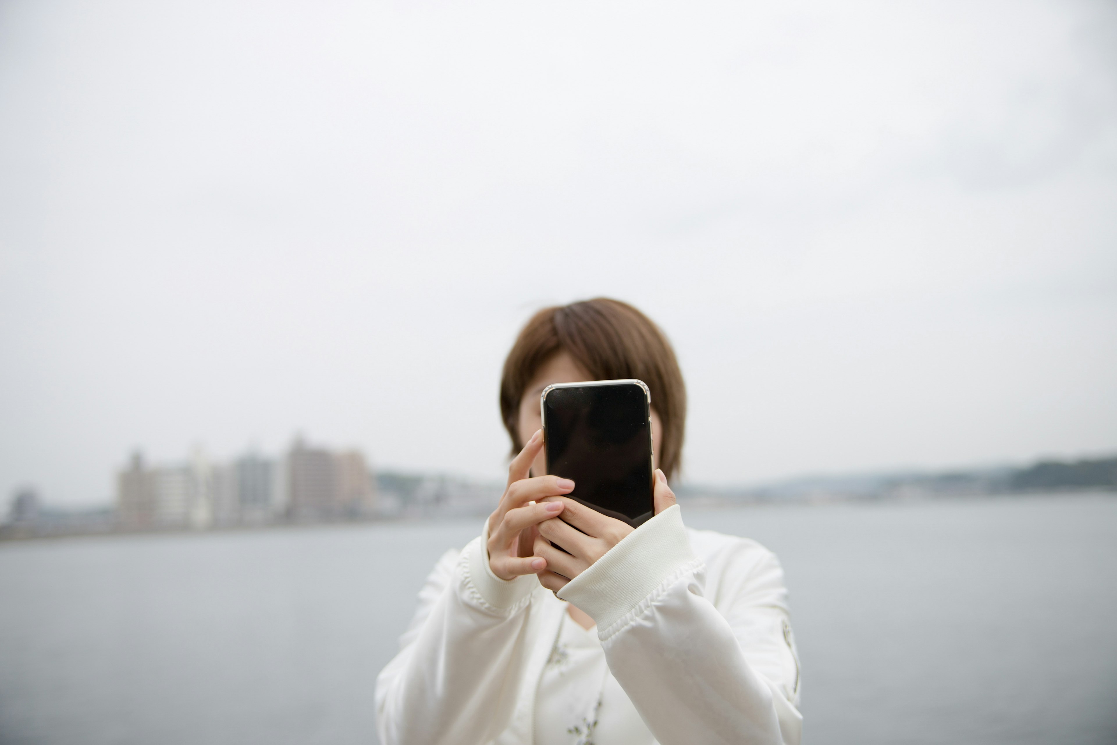 Porträt einer Frau, die ein Smartphone vor einem Gewässer hält