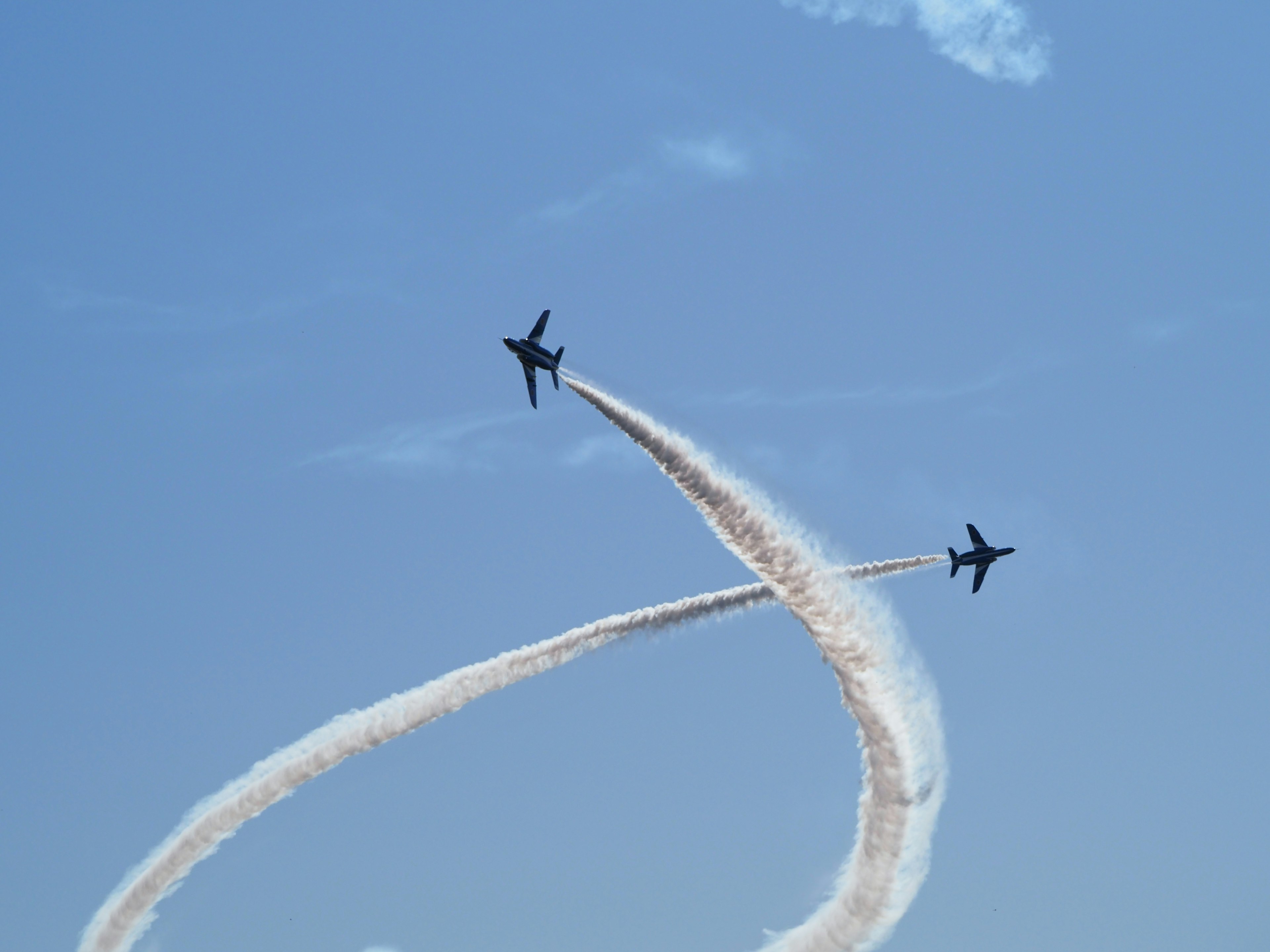 Two fighter jets flying in a curved formation against a blue sky leaving smoke trails