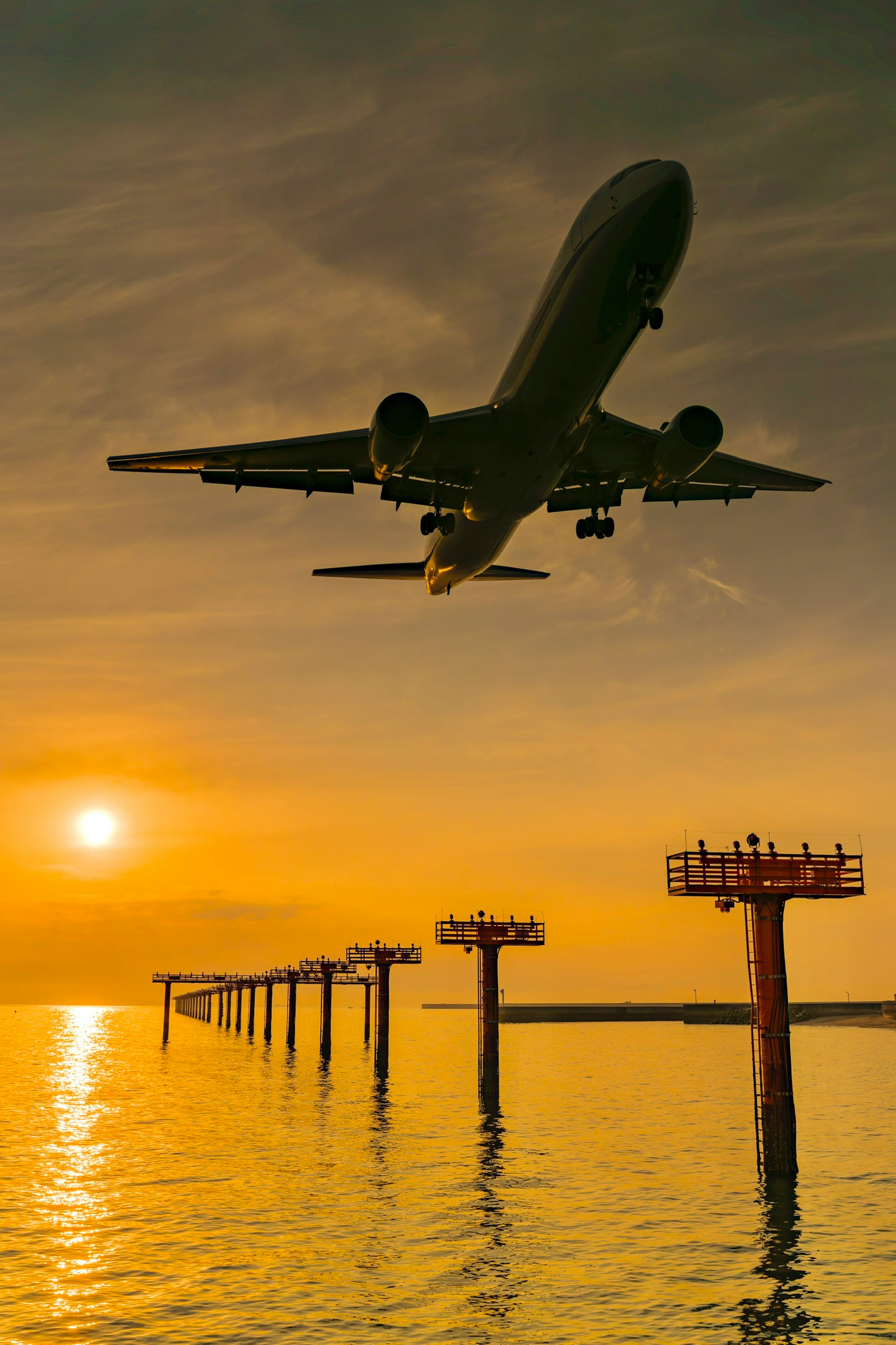 An airplane flying against a sunset background with a pier in the water