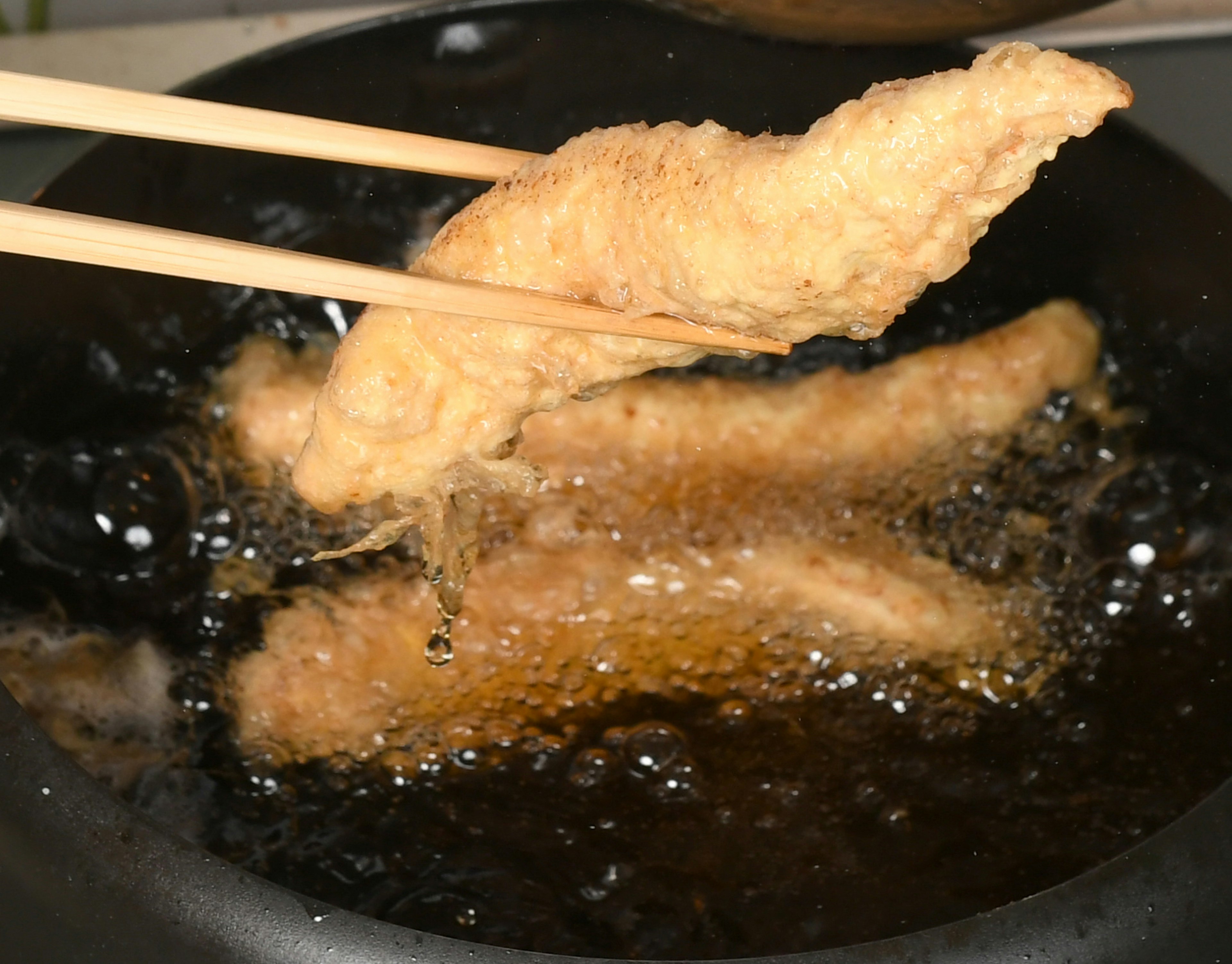 Fillet ikan goreng diangkat dengan sumpit dari minyak panas