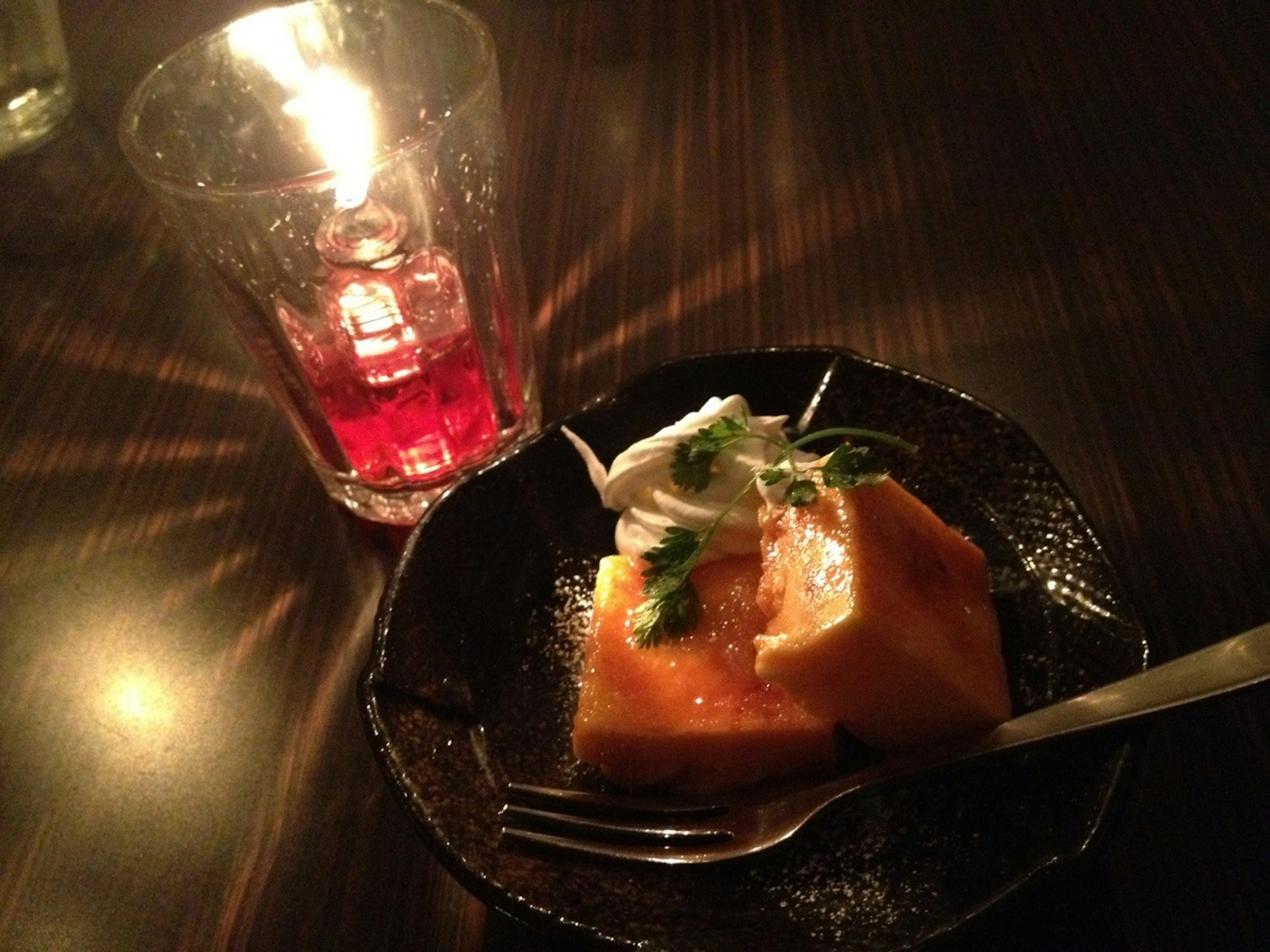 Un dessert dans une assiette avec une boisson rouge dans un verre éclairé par la lumière des bougies