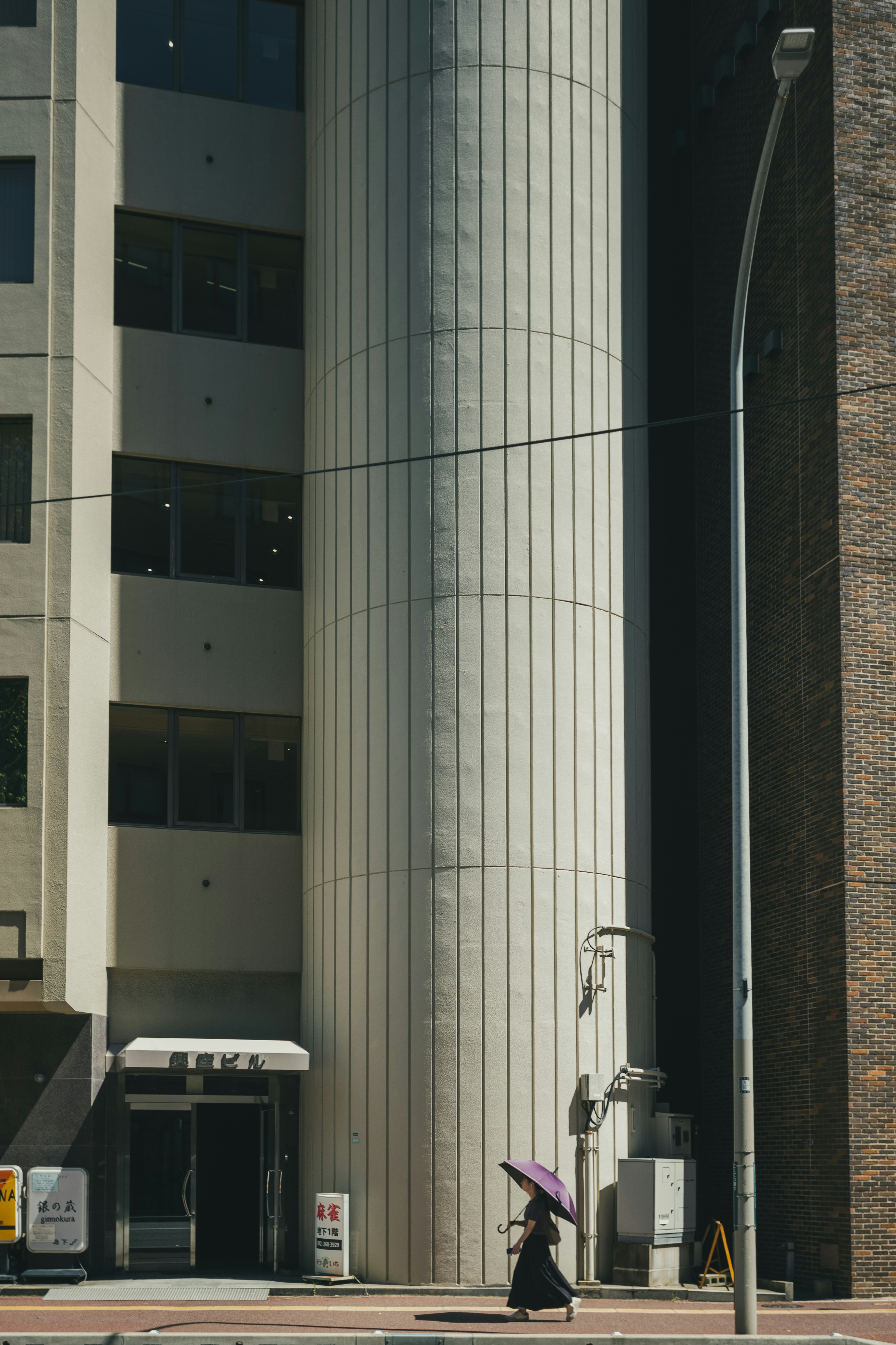 A person holding an umbrella stands by a concrete pillar next to a modern building