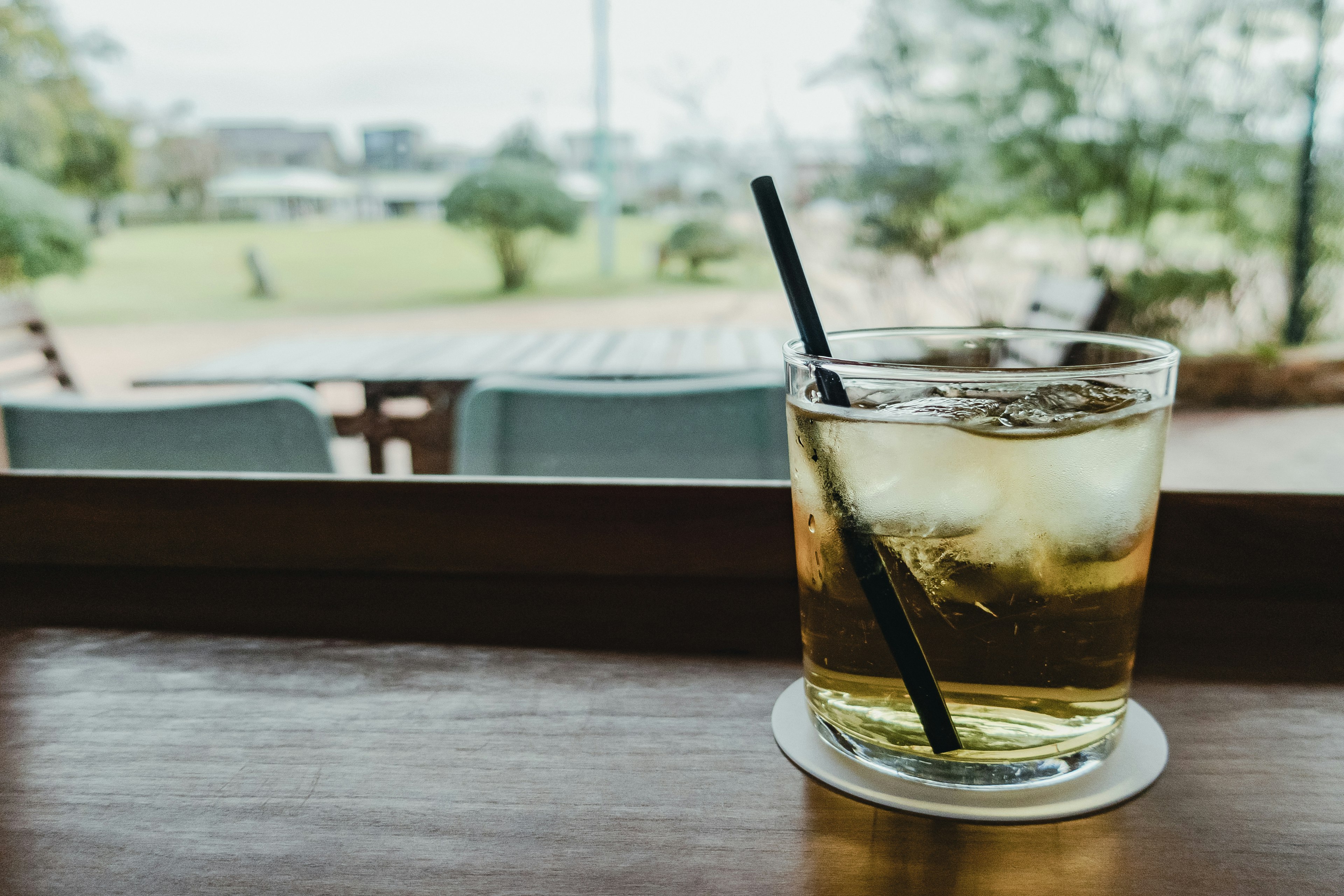 Ein Glas mit Eisgetränk auf einem Cafétisch mit Blick auf den Garten draußen