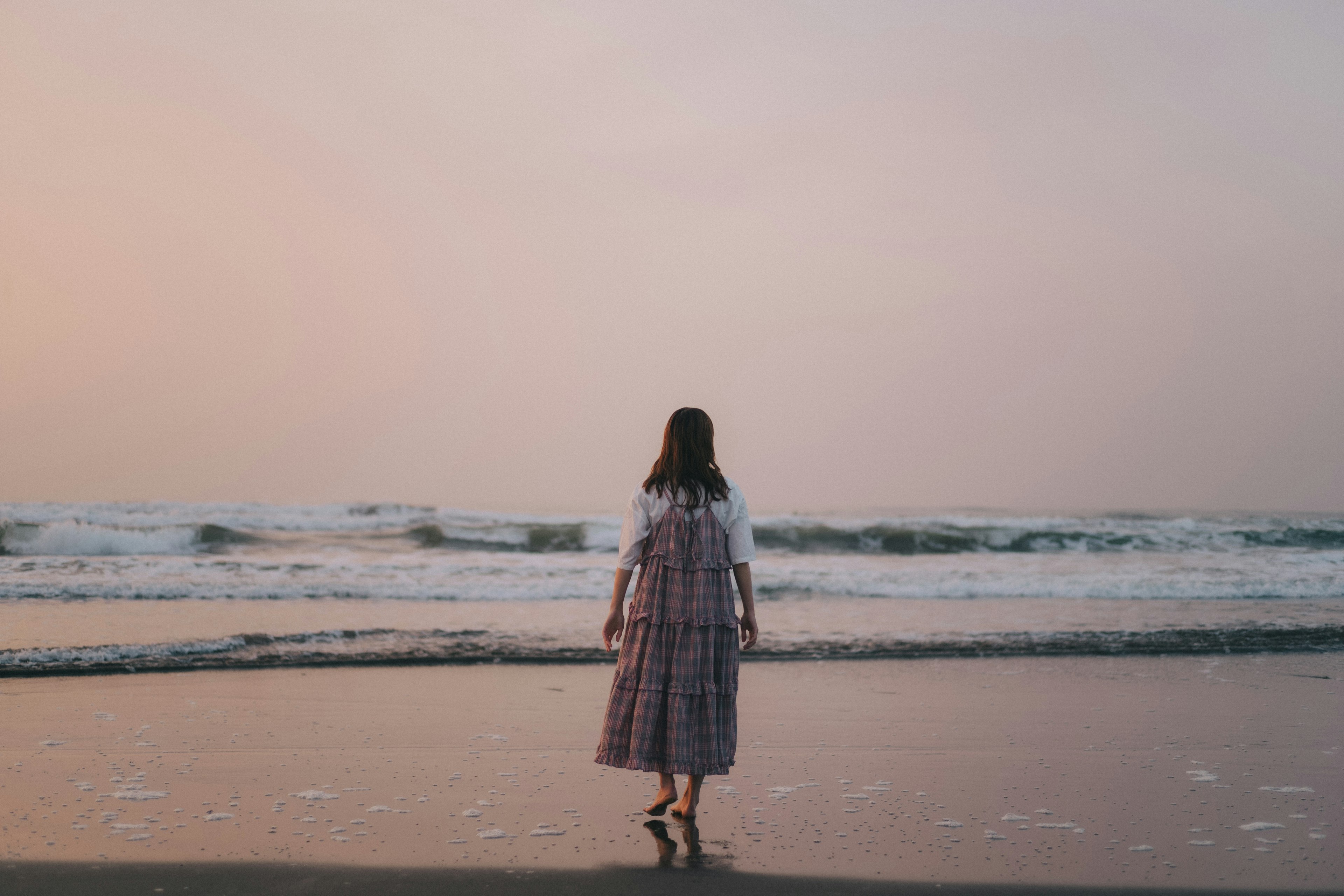 Donna in piedi sulla spiaggia che guarda l'oceano al tramonto