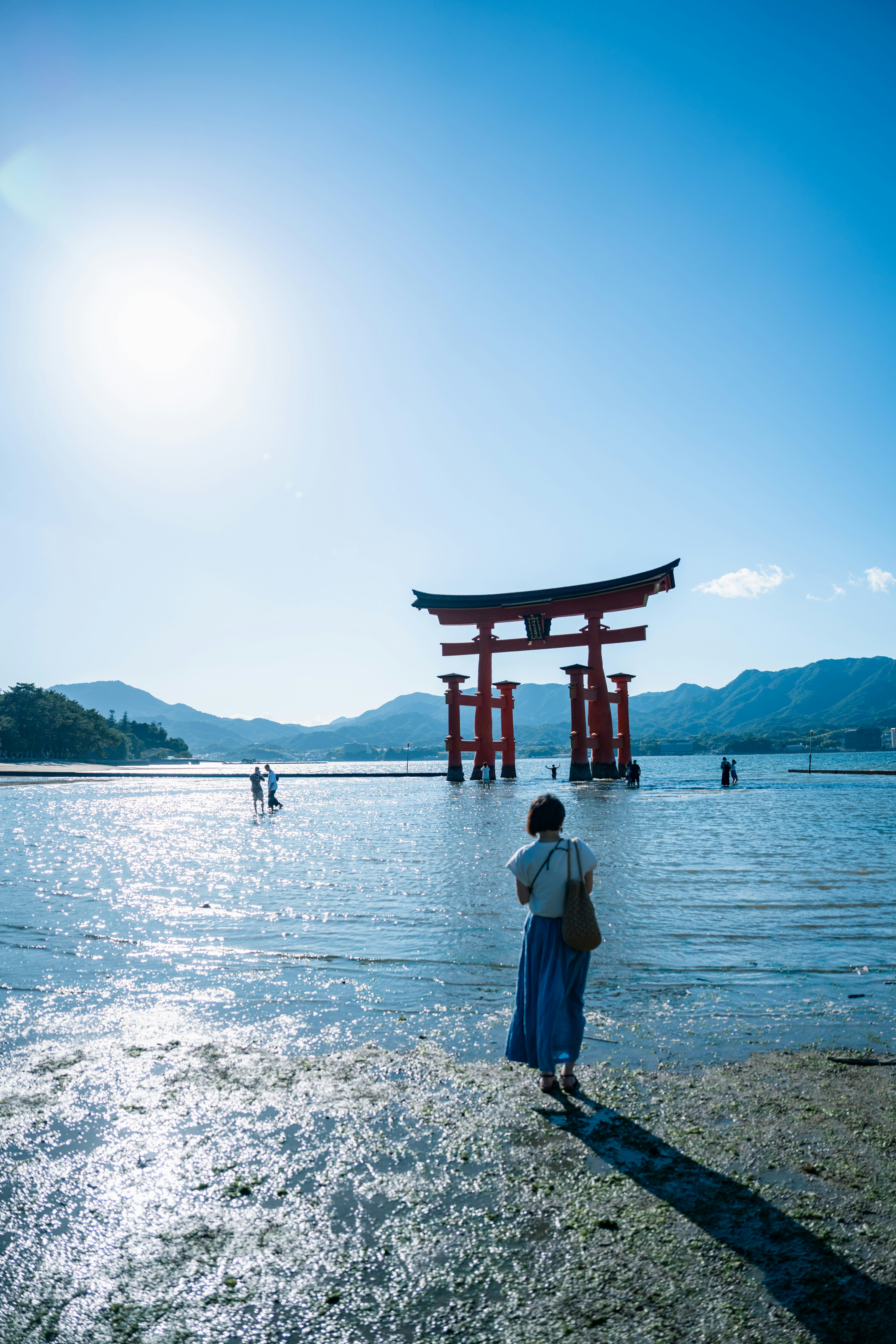 Un torii se tenant dans l'eau peu profonde avec une femme faisant face