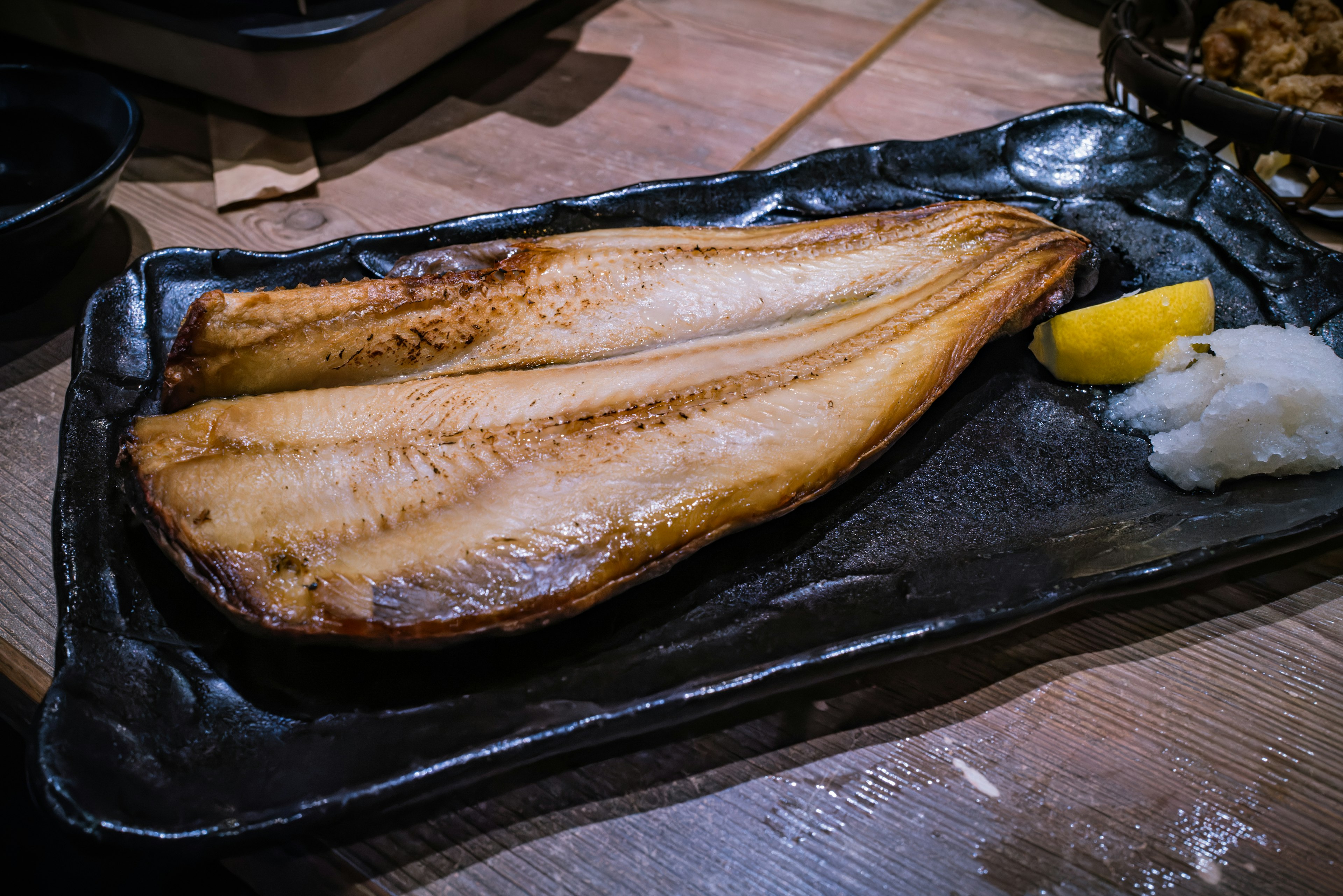 Poisson grillé servi sur une assiette noire avec du citron et du radis râpé