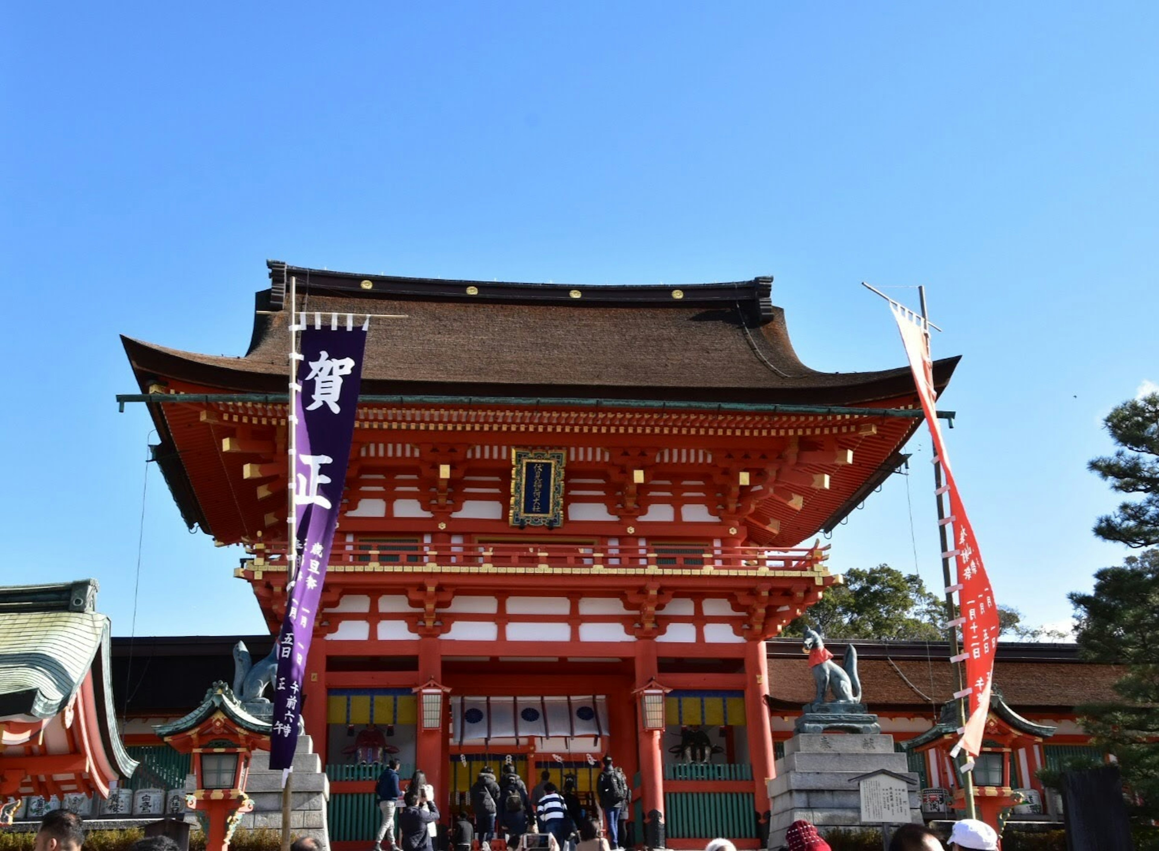 A beautiful red shrine building with people gathered under a clear blue sky