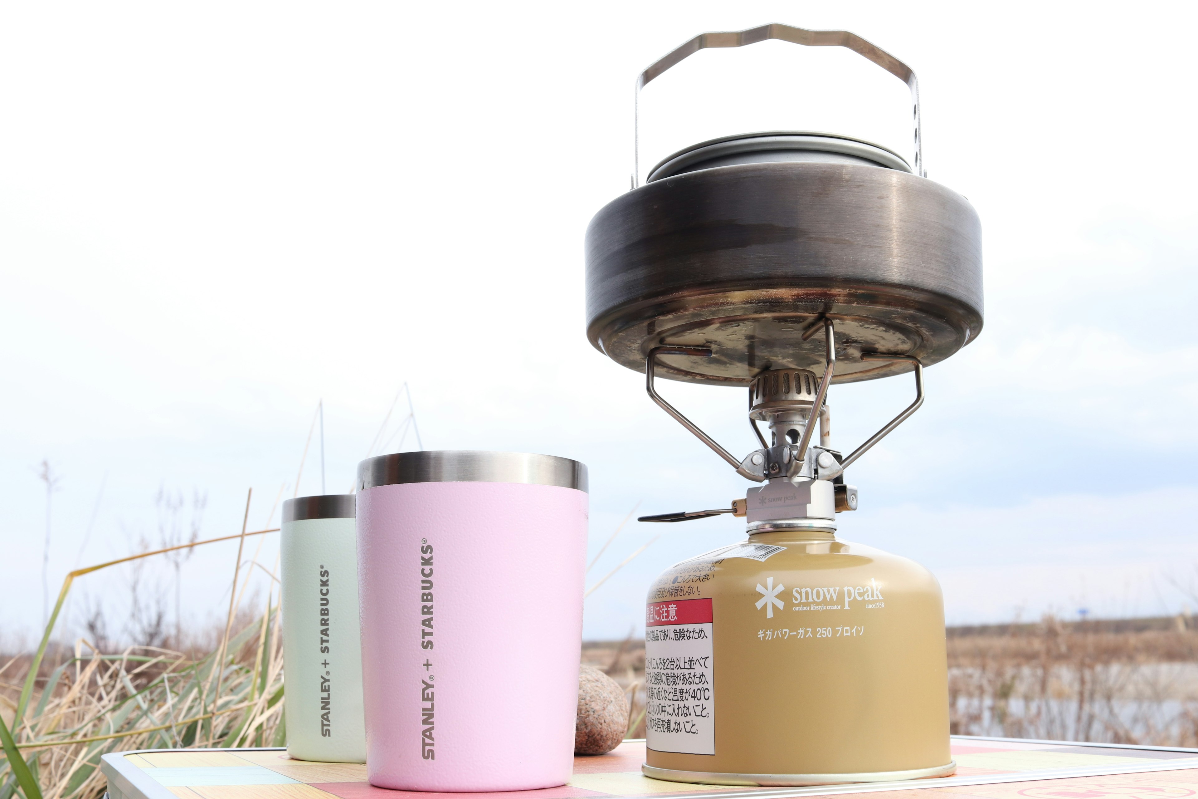 Outdoor gas stove with colorful mugs displayed in a natural setting