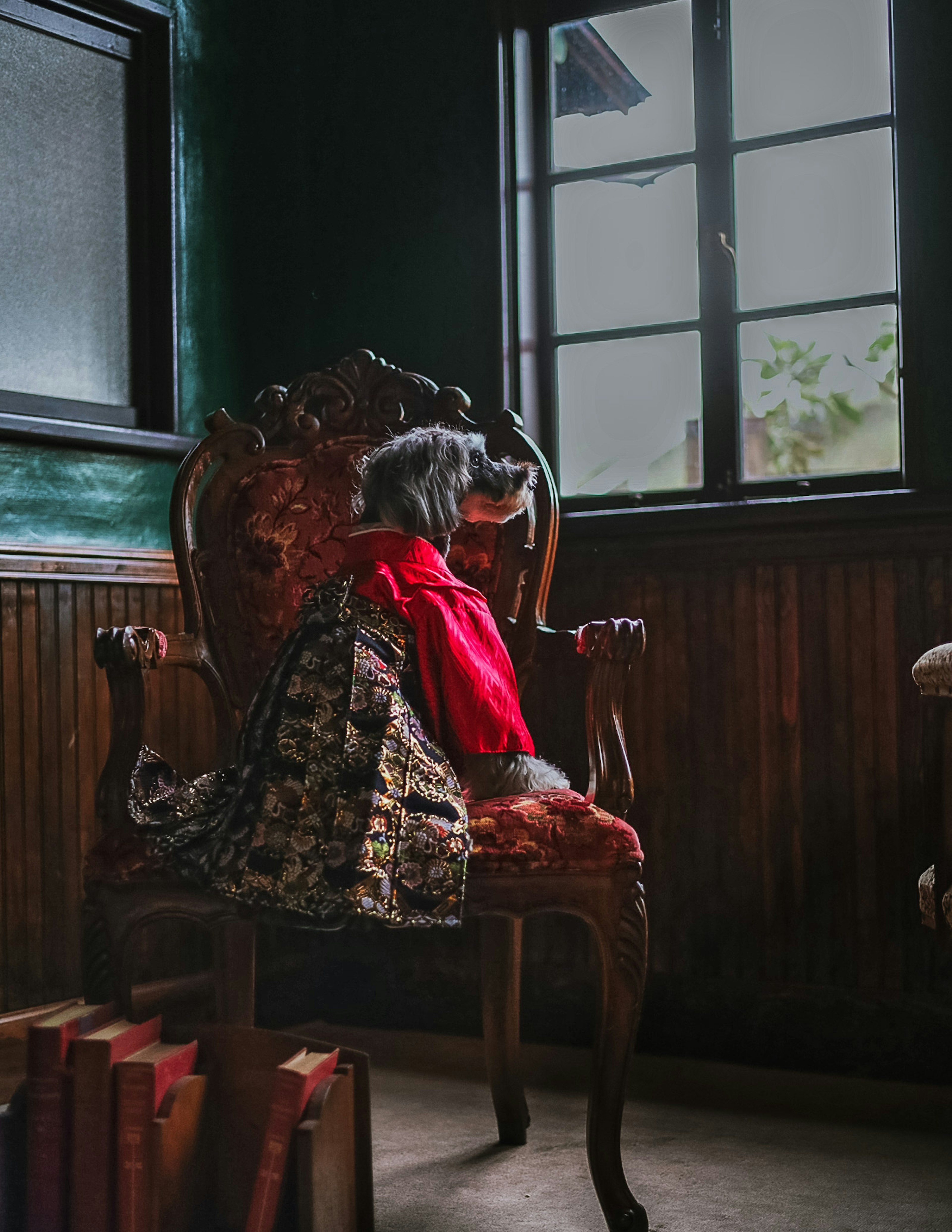 A doll in a red dress sitting on an ornate chair in a dimly lit room