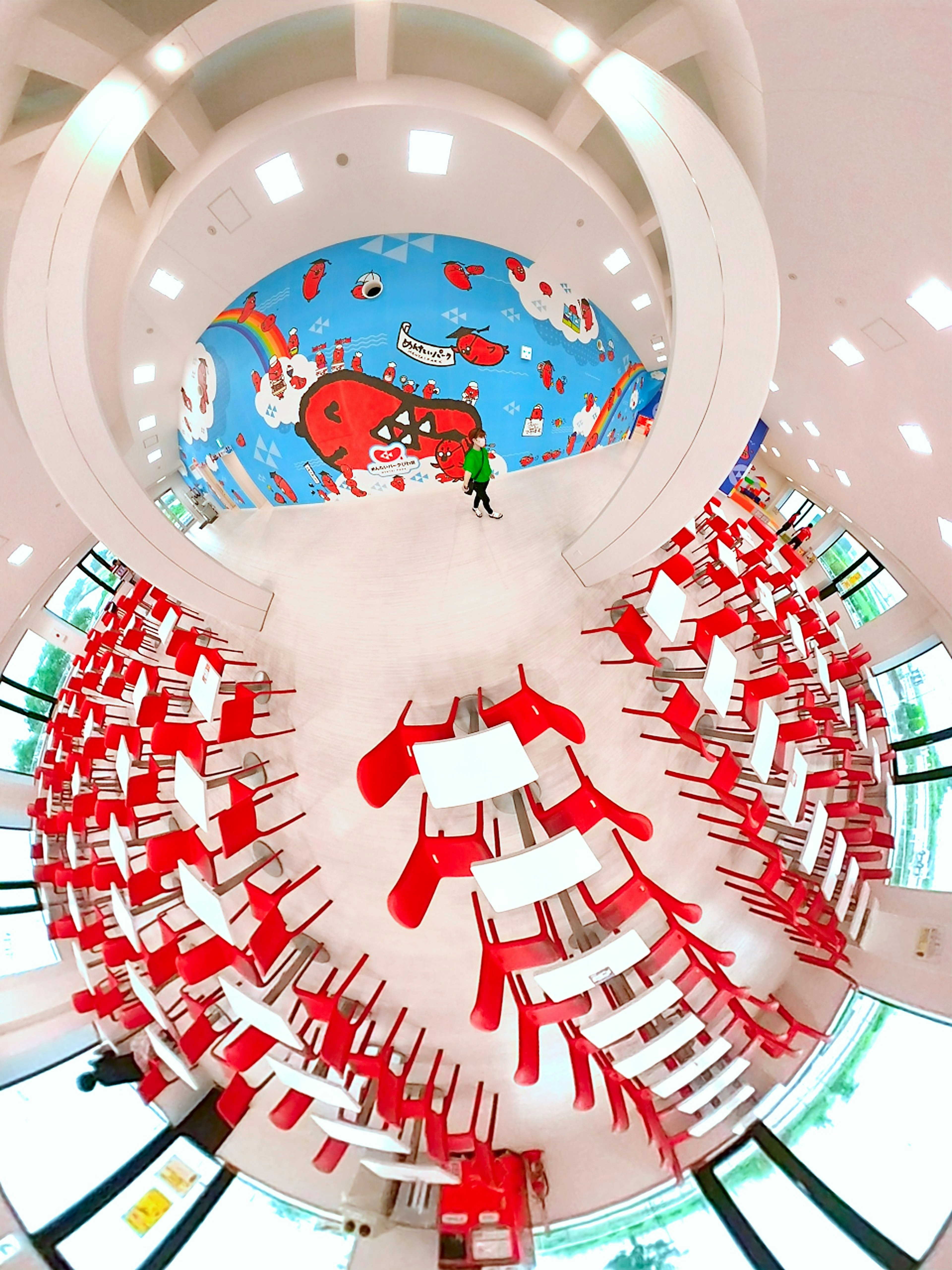 Interior of a classroom with red chairs and white tables featuring colorful wall art