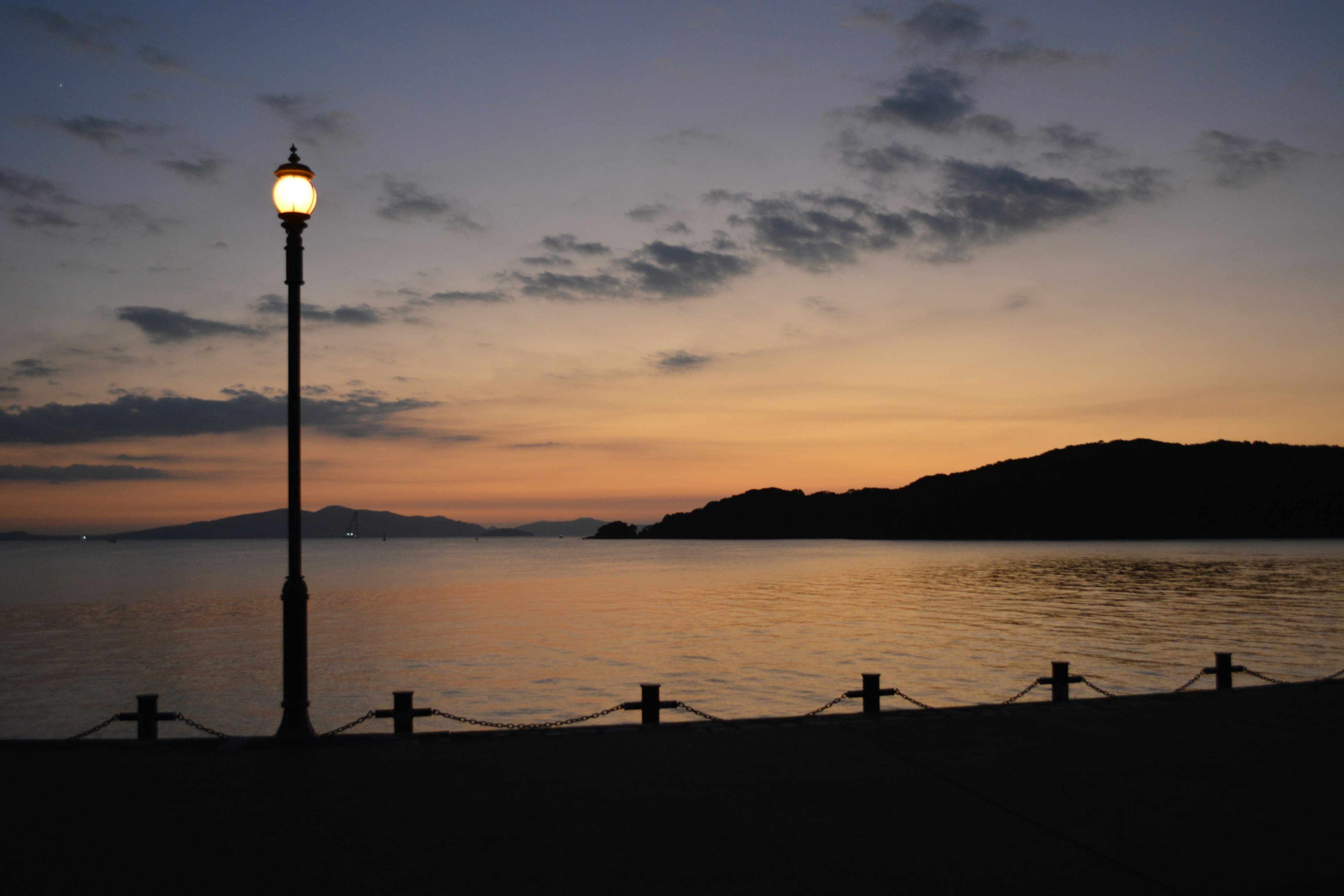 夕焼けの海岸に立つ街灯と穏やかな水面