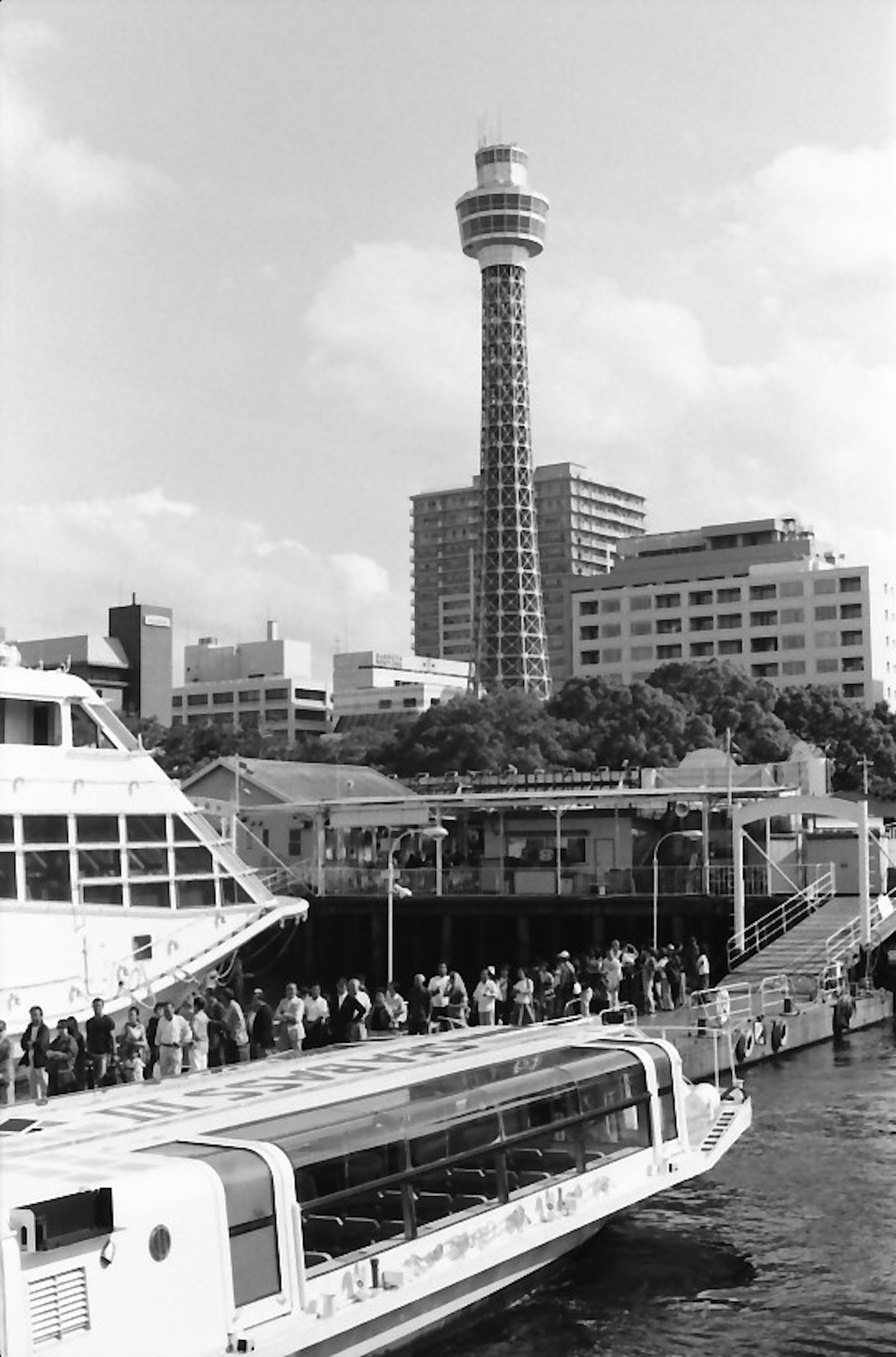 Immagine in bianco e nero di una barca ormeggiata al porto di Yokohama con la Torre Marina di Yokohama sullo sfondo