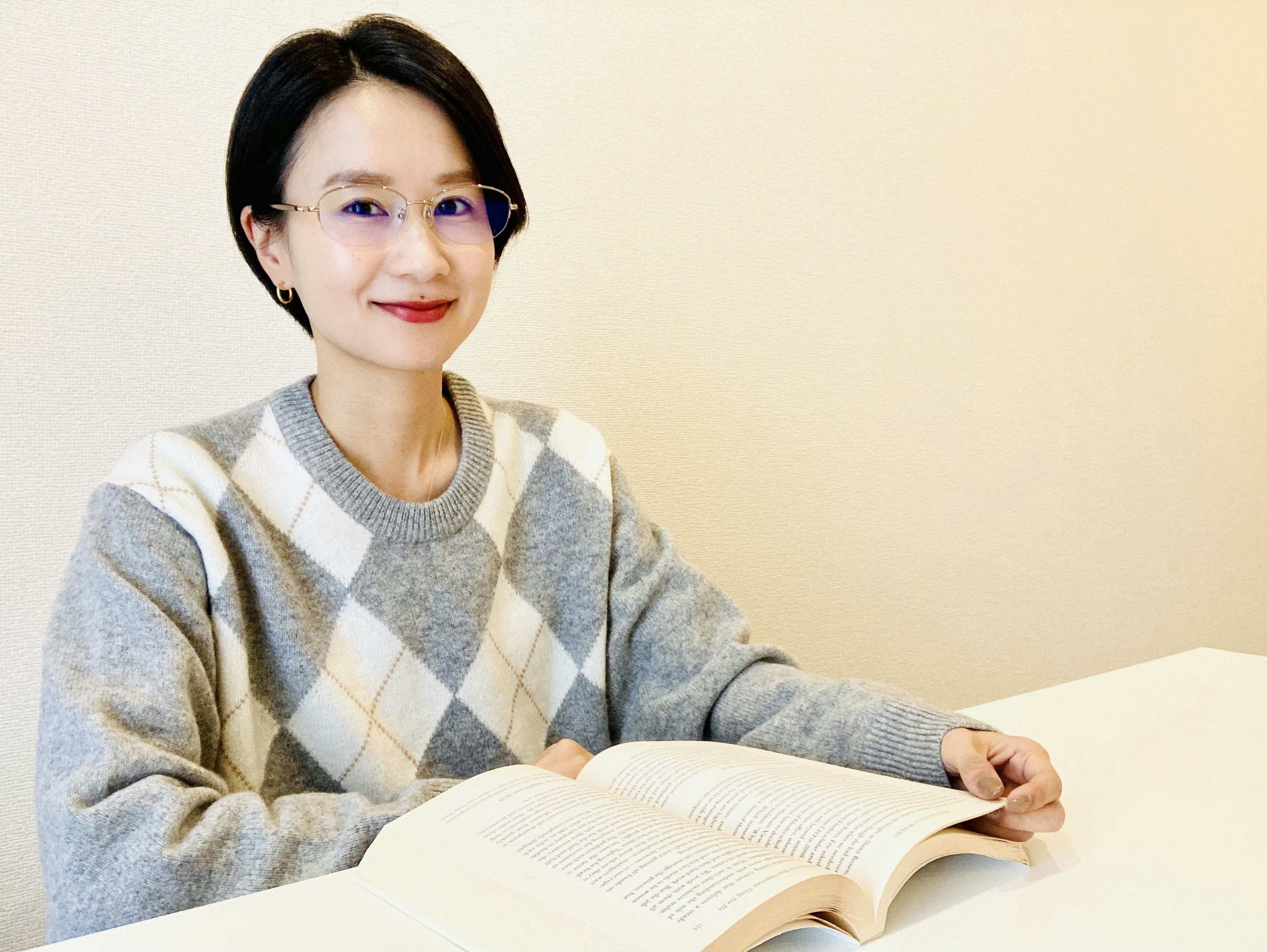 Una donna sorridente che tiene un libro indossando un maglione grigio