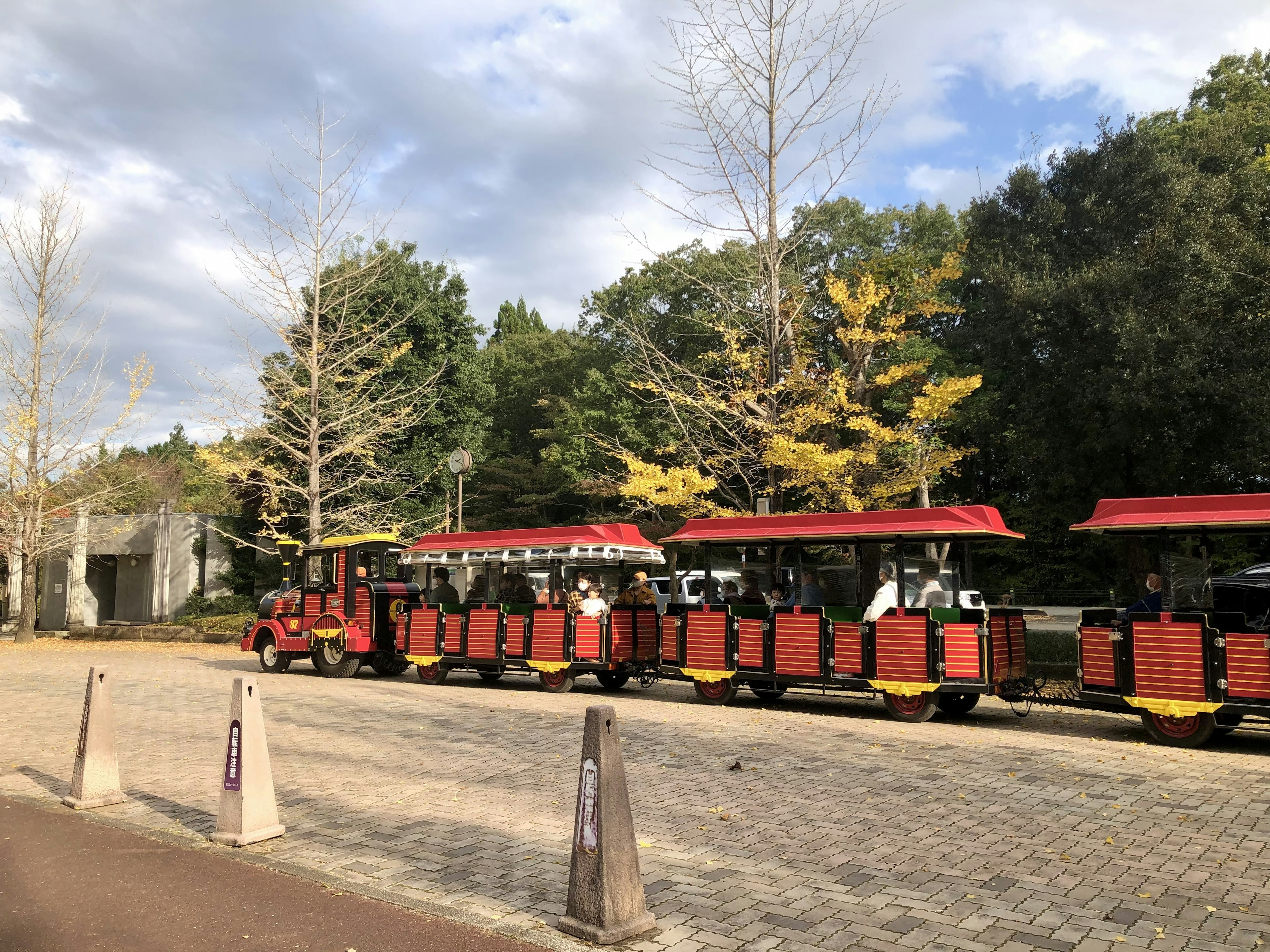 A scene featuring a tram with a red roof parked along a pathway surrounded by green and yellow trees