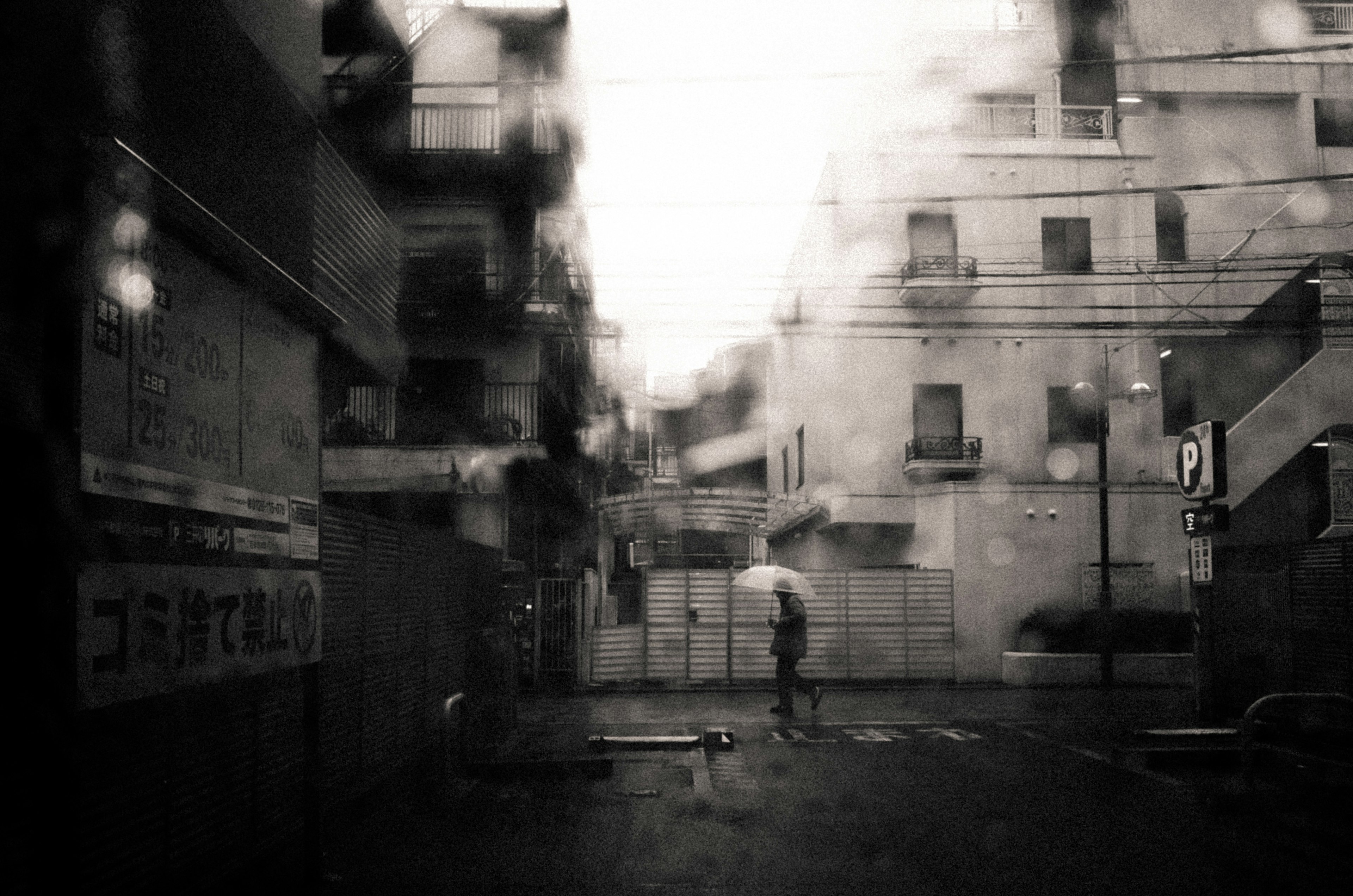 Verschwommene Stadtlandschaft im Regen mit einer Person, die einen Regenschirm hält