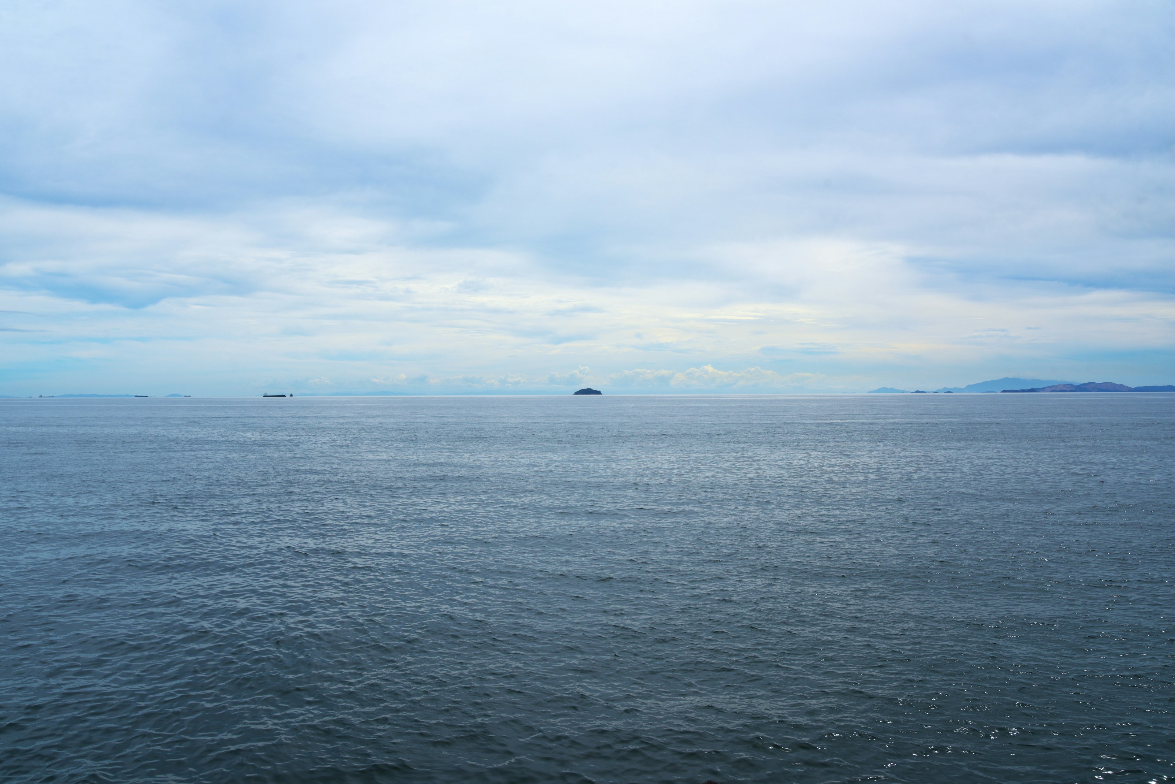 Expansive view of blue ocean under a cloudy sky with distant ships