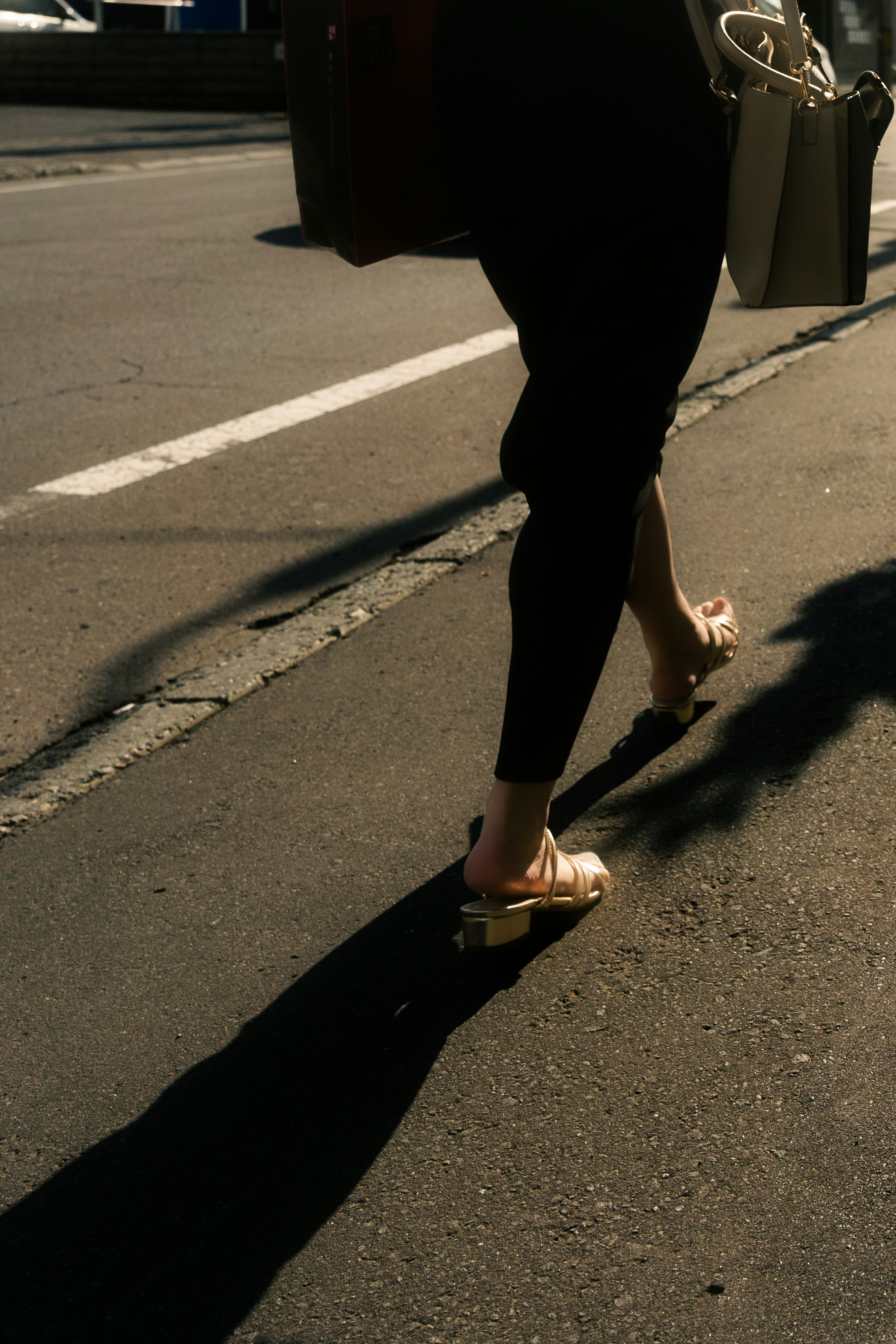 A person's feet walking on the street with a shadow cast on the pavement